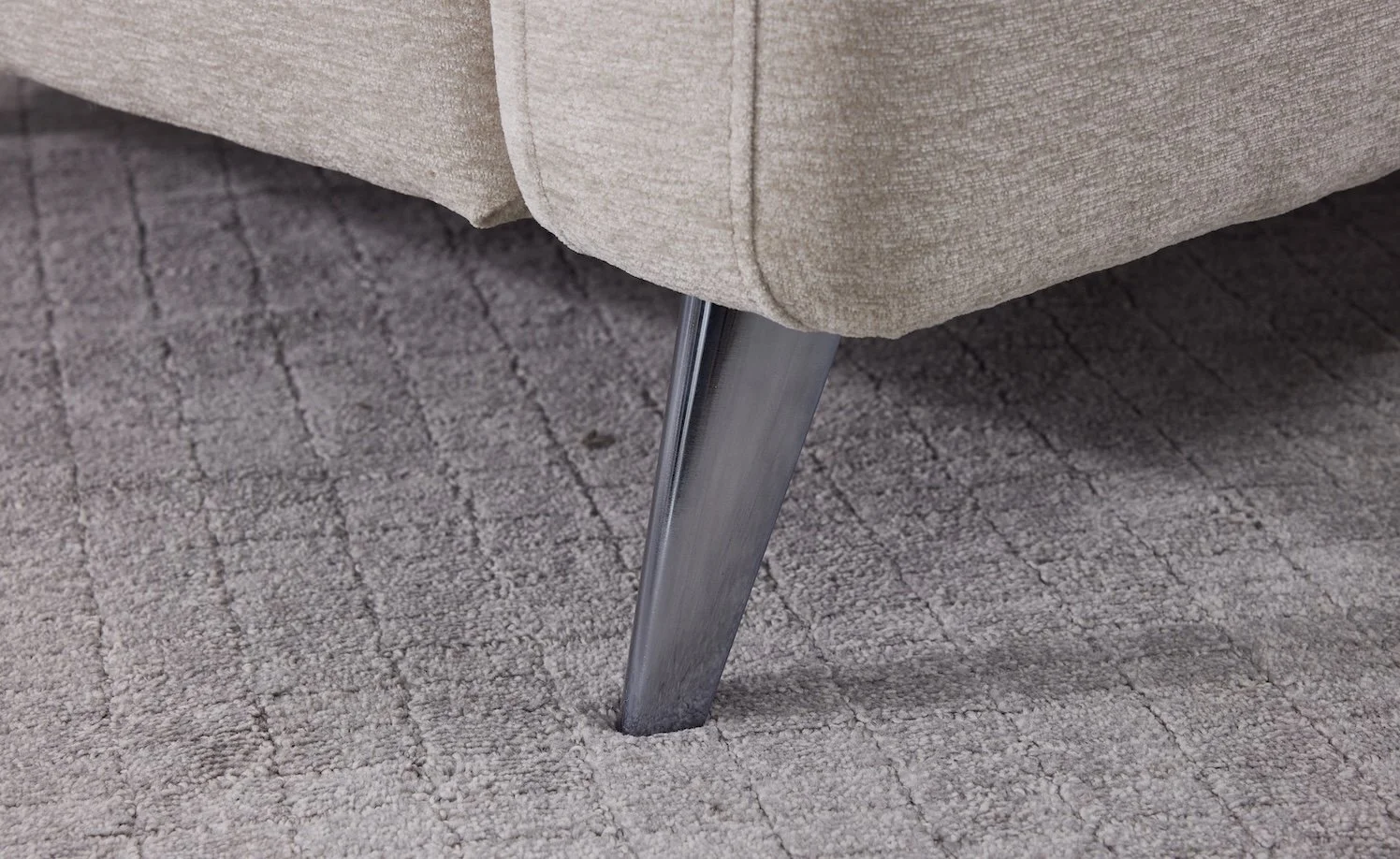 Close-up of a light beige upholstered sofa with metal legs, standing on a textured hardwood floor.