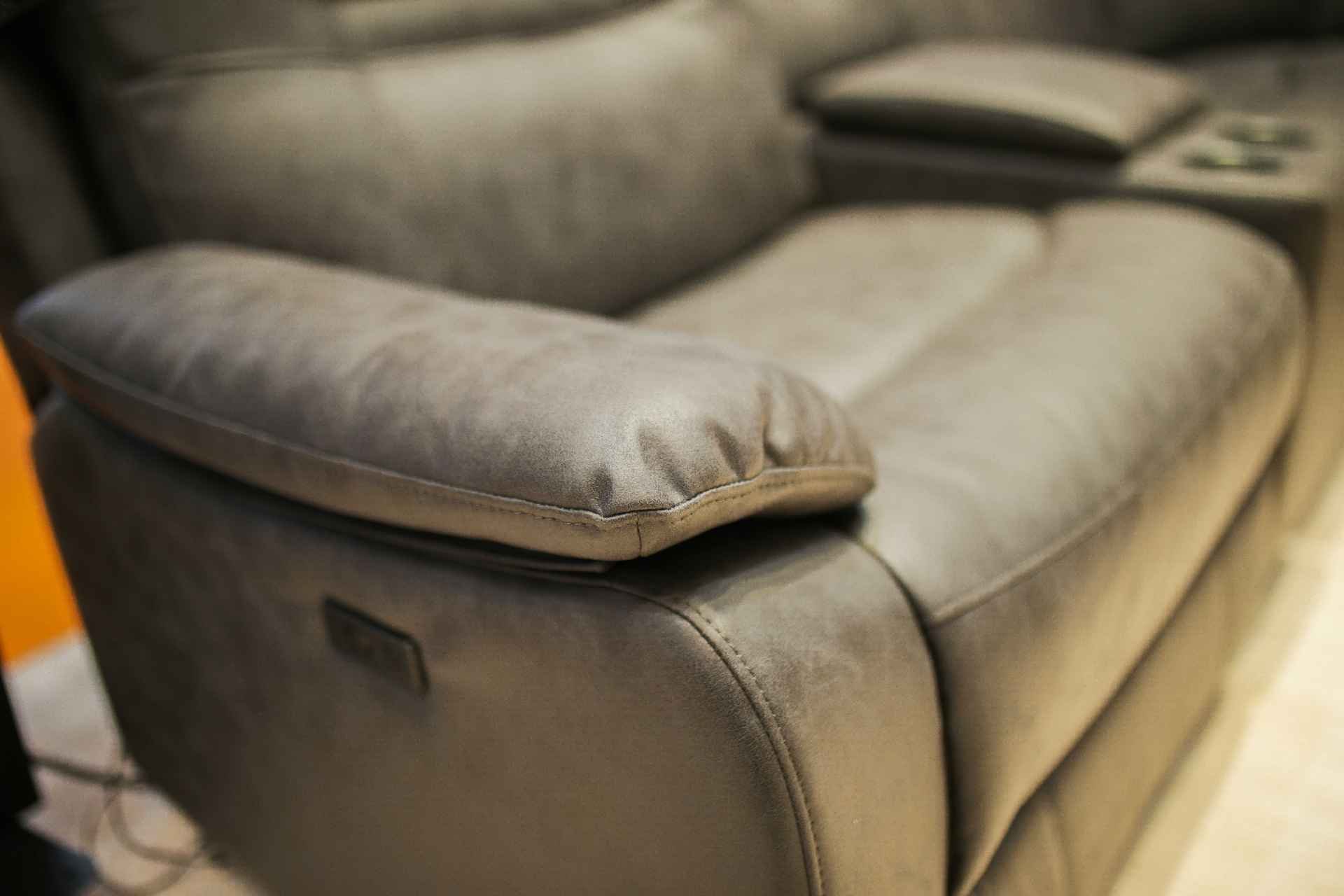 Close-up of a beige upholstered sofa with a plush armrest and visible stitching.