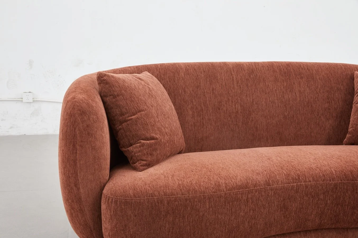 A rust-colored upholstered sofa with matching cushions against a plain white wall.