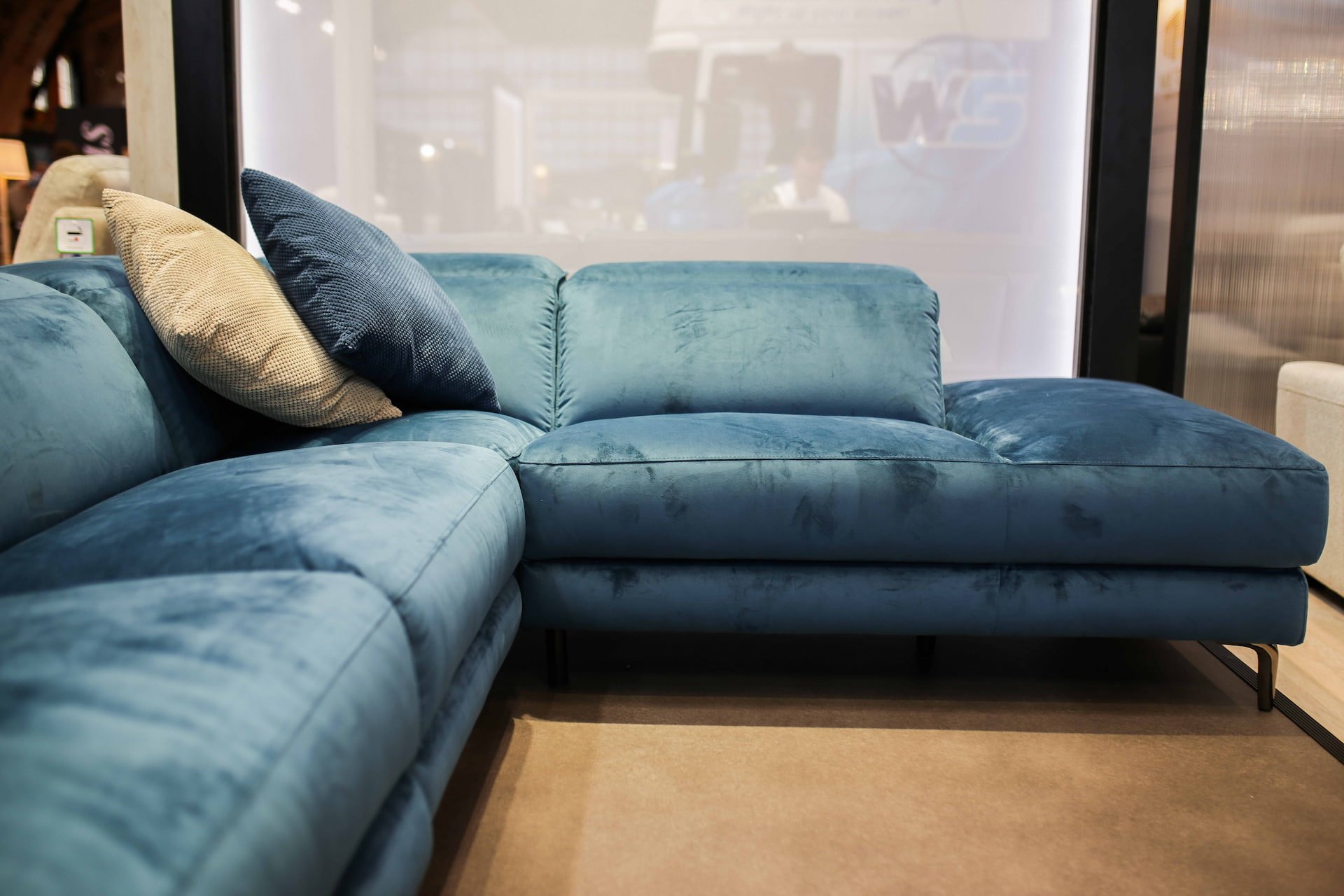 Blue velvet sectional sofa with a beige and a blue pillow on it, in a furniture store display area.