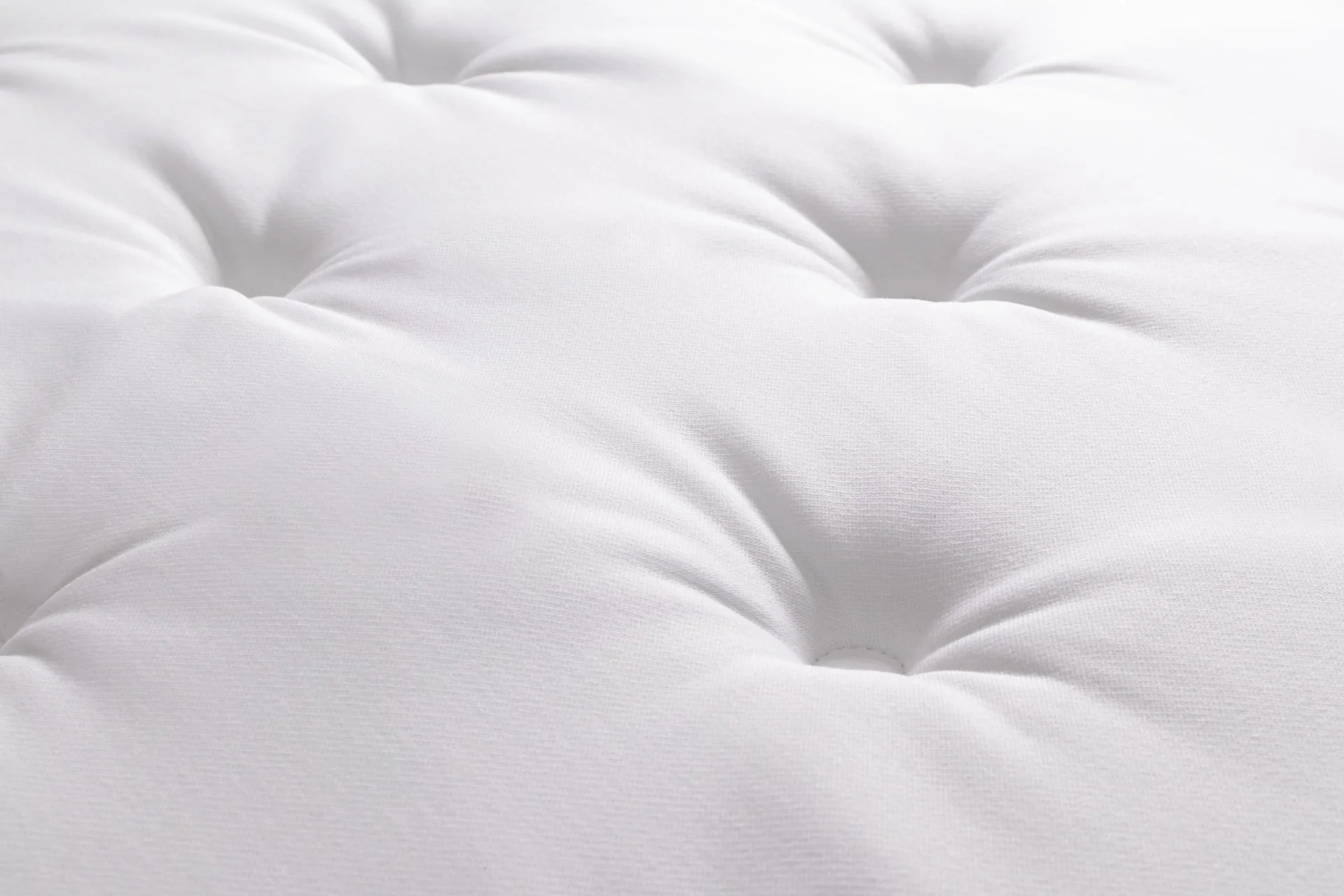 Close-up of a white, tufted, soft mattress surface with button indentations.