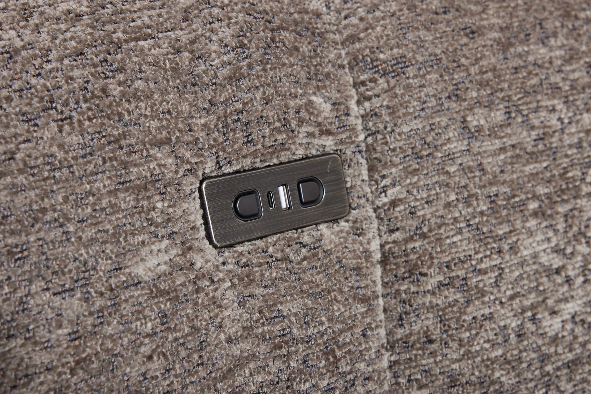 Close-up of a beige and brown textured carpet with an electrical outlet and switch plate