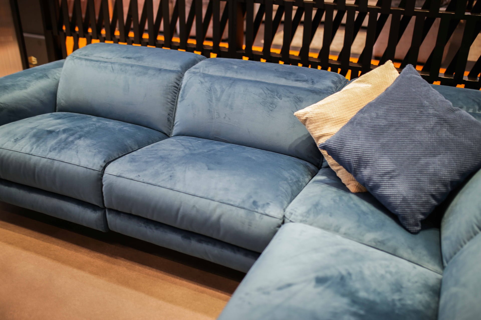 A blue velvet sectional sofa with two throw pillows, one beige and one dark blue, in a living room setting.