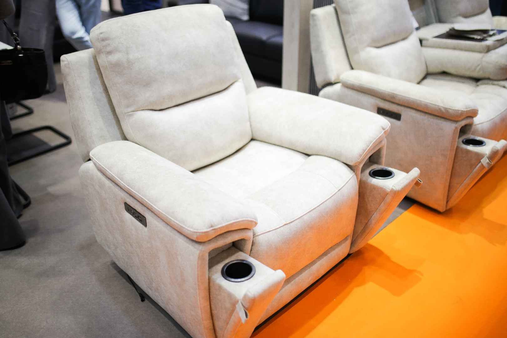 Two beige recliner chairs with built-in cup holders on the armrests, displayed in a furniture store.