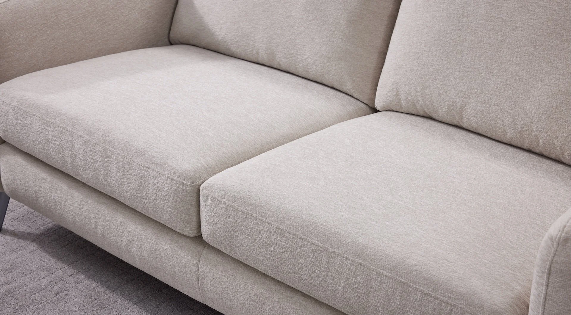 Close-up of a beige upholstered sofa with cushions on a matching rug.