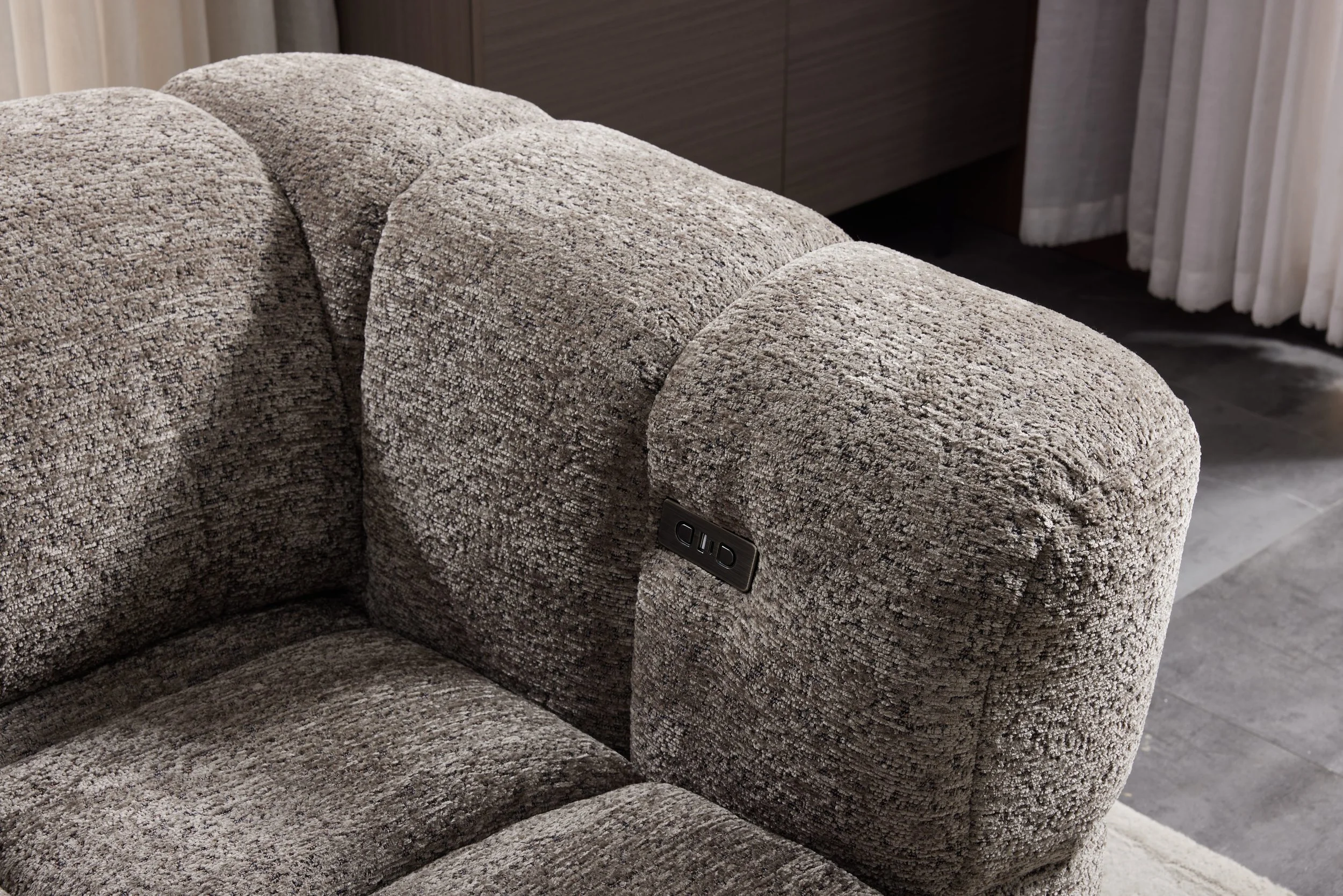 A close-up of a beige, textured upholstered sectional sofa with tufted cushions in a modern living room.
