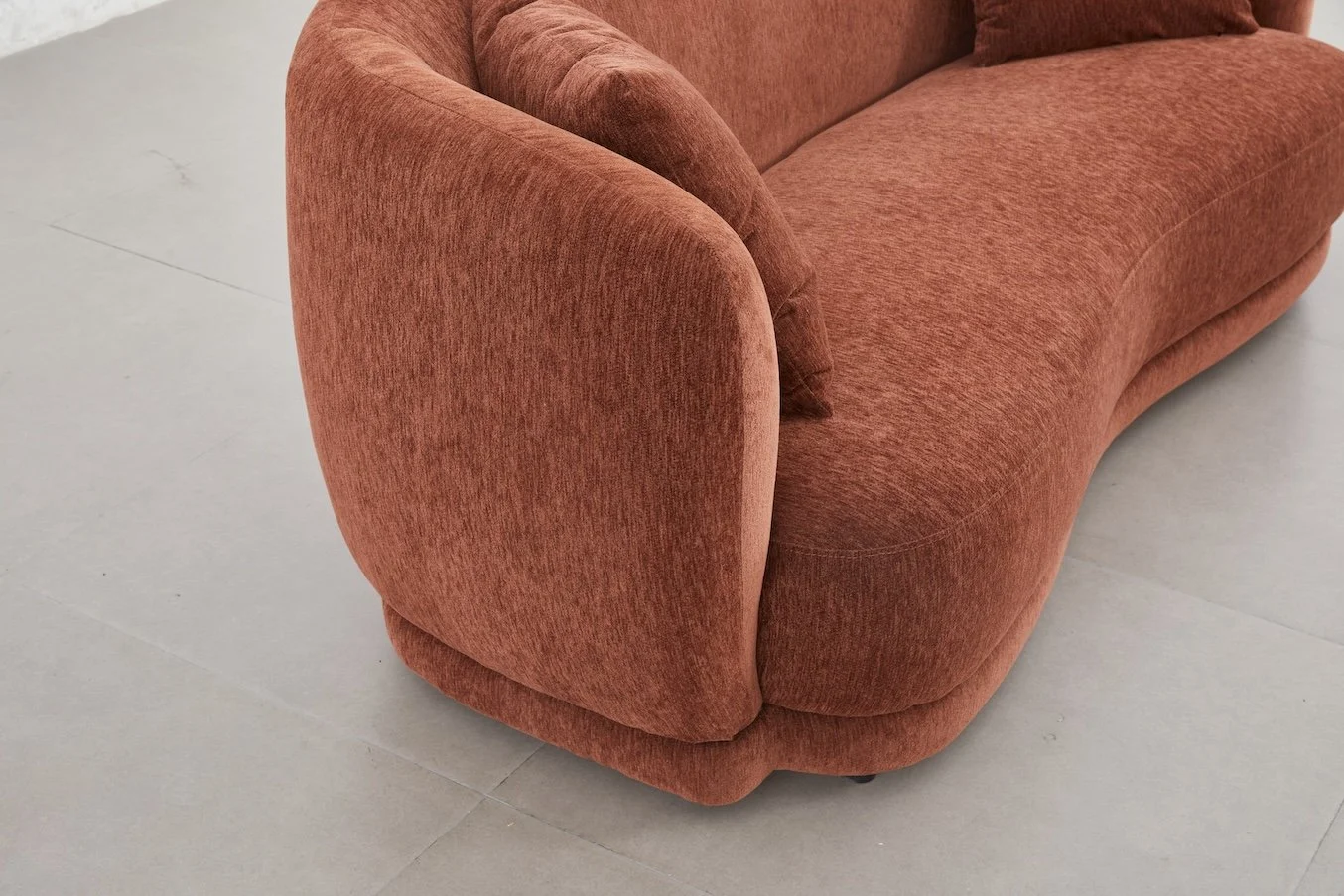 Close-up of a red-orange curved sofa with matching cushions on a light-colored tiled floor.