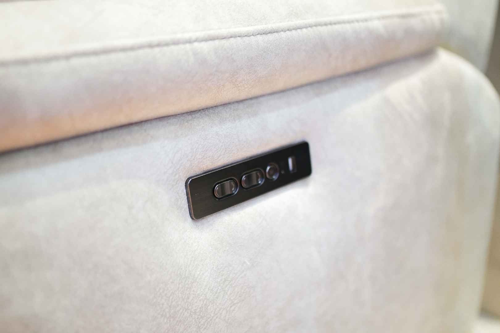 Close-up of a control panel embedded in the back of a beige upholstered seat, featuring four black buttons.