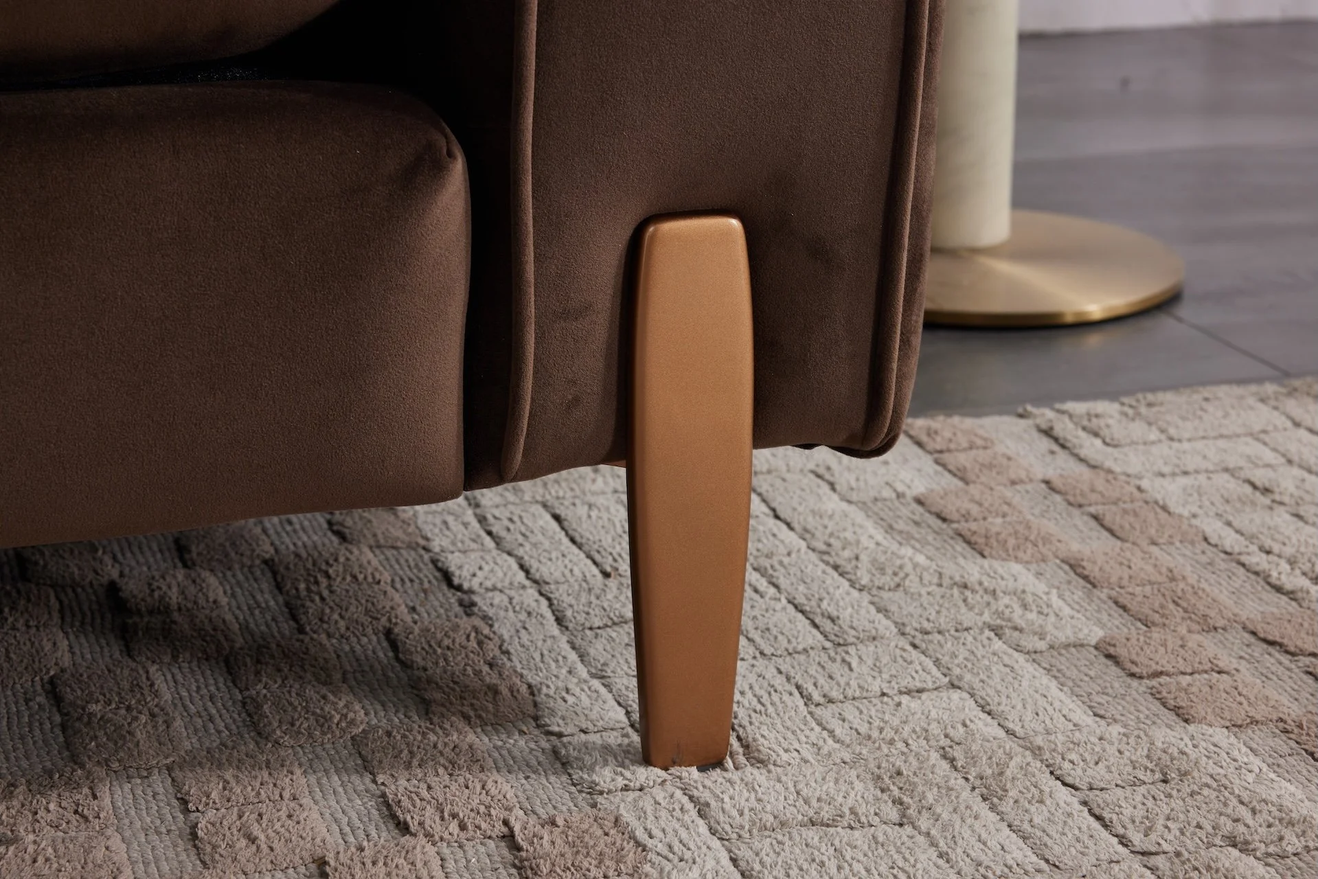 Close-up of a wooden furniture leg supporting a brown upholstered chair or sofa on a beige and light brown textured rug.
