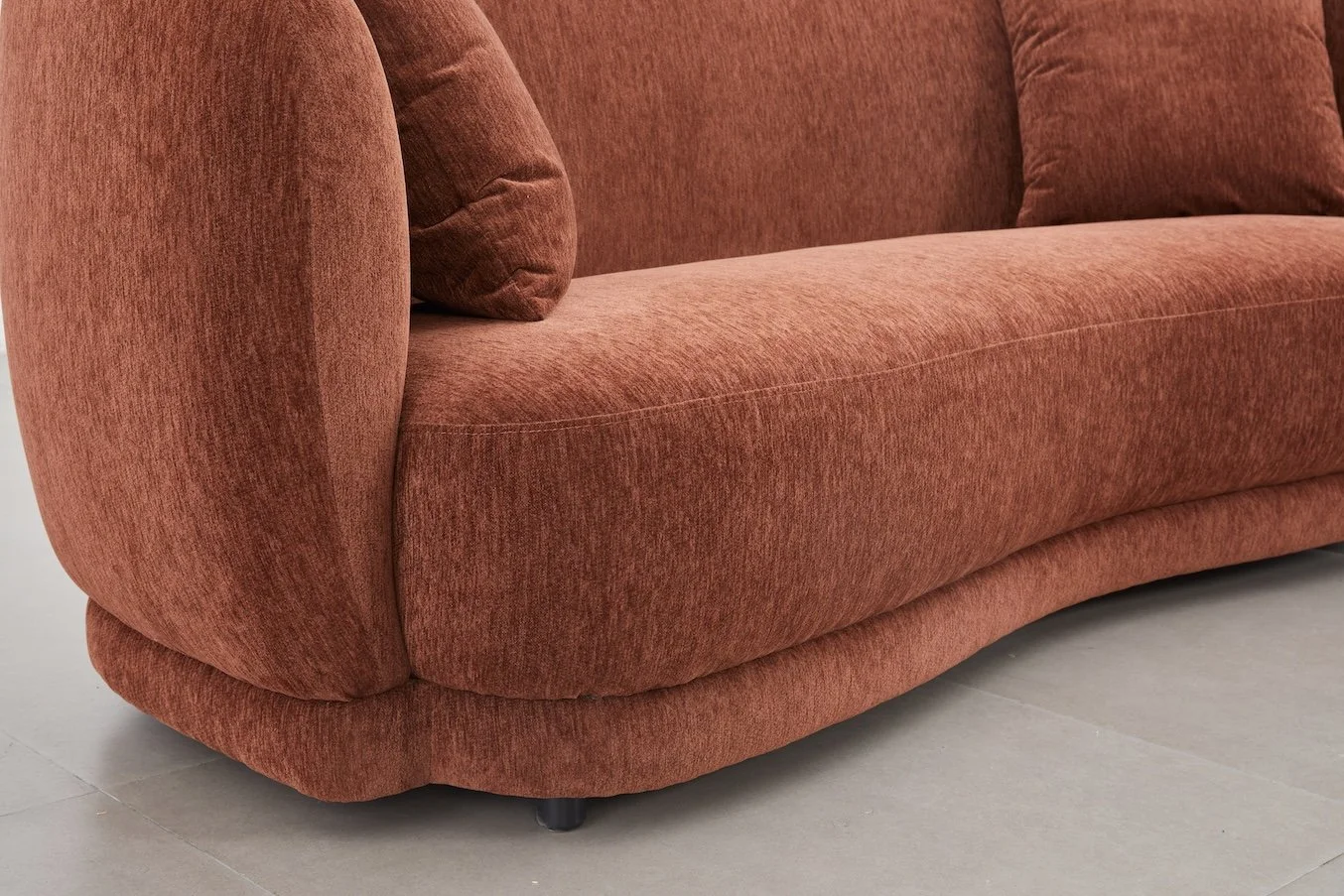 A close-up of an orange-brown upholstered sofa with a matching pillow, showing the side and part of the seat cushion, on a light-colored tiled floor.