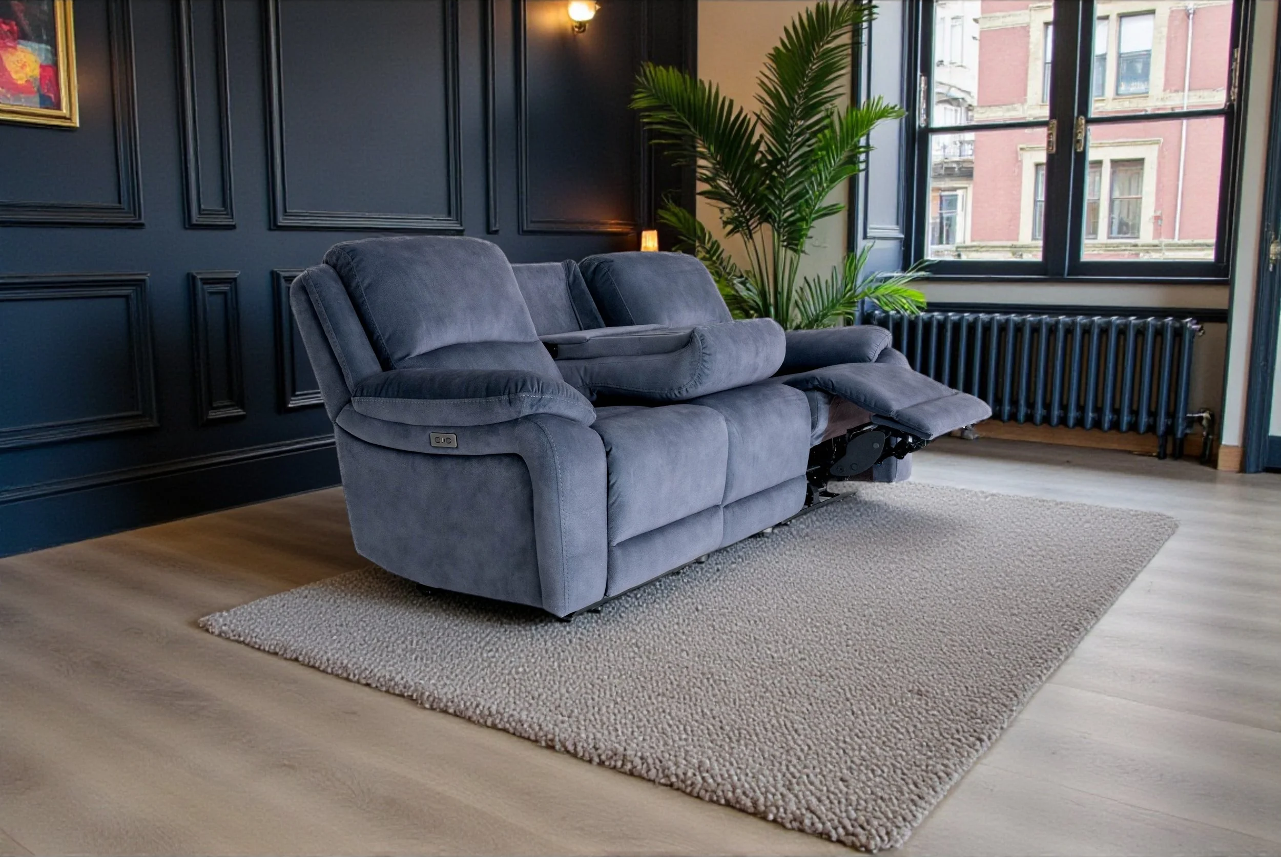 A dark gray fabric couch with three cushions and rolled armrests, set against a plain white background.