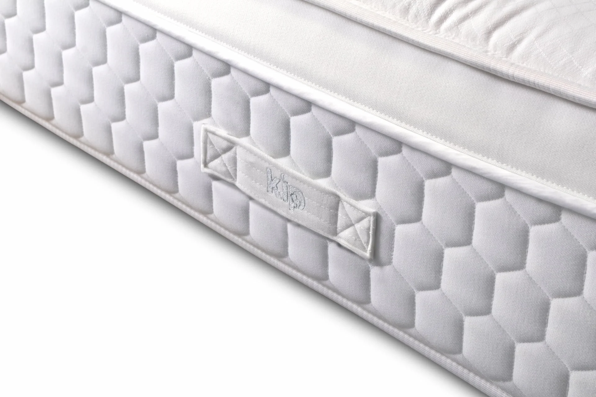 Close-up of a white mattress featuring a hexagonal quilted pattern and a fabric label with the brand name 'Kip' stitched onto the side.