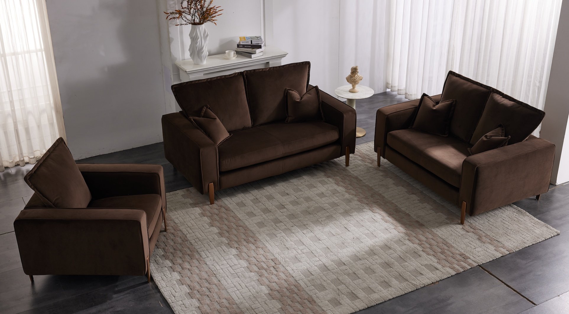 Living room with three brown couches, a beige patterned rug, a white side table with a classical bust, a white mantle with books and a vase with branches, and white curtains on large windows.