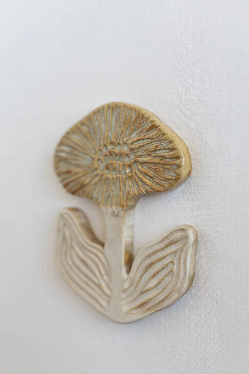 Kuvassa on saviveistos, joka muistuttaa sientä, ja se on kiinnitetty valkoiselle taustalle.