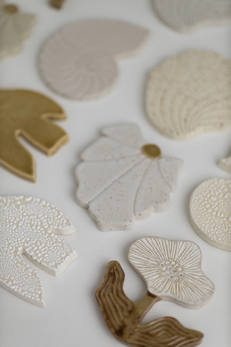 Läpinäkyviä ja kermanvärisiä kauniita muotoiltuja keramiikkalevyjä ja -siruja, osa niistä on koristeellisia ja osa geometrisia, aseteltuna valkoiselle taustalle.