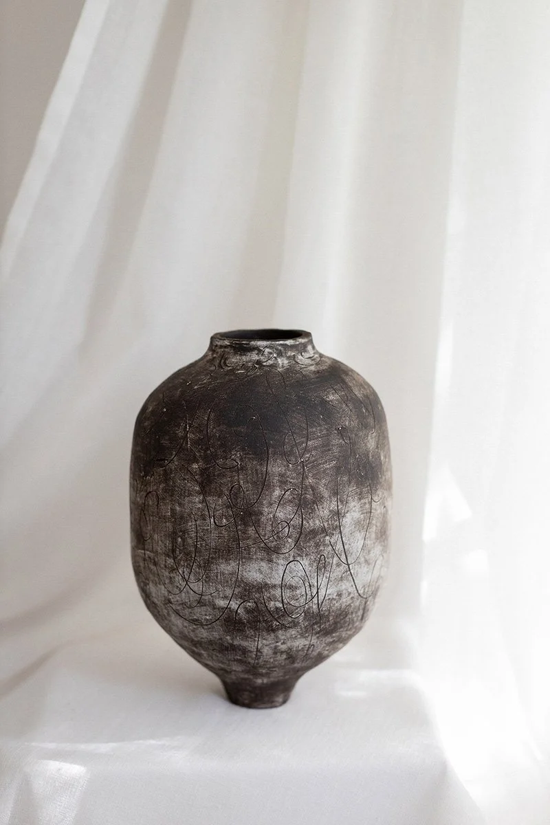 Keramiikka-astia, harmaa ja runsaasti koristeellisia muotoja ja piirettyjä viivoja, asetettuna valkoiselle pinnalle valkoinen tausta.