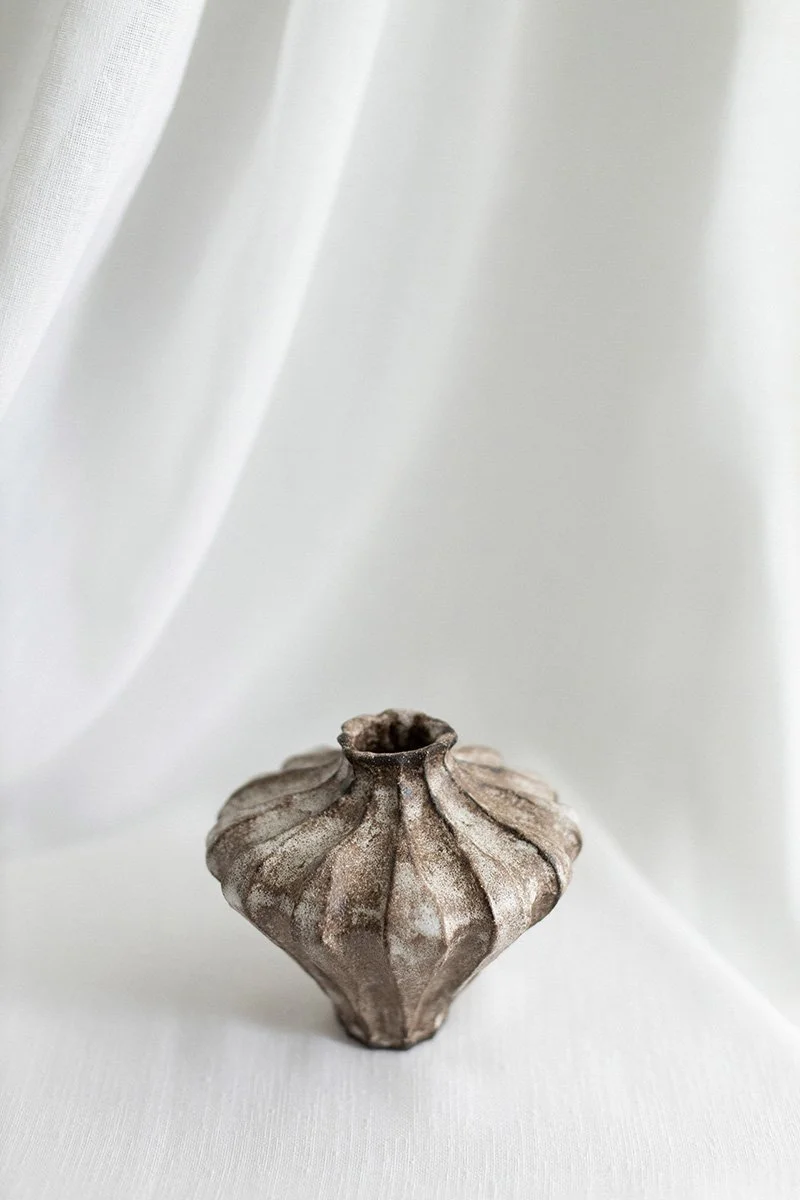 Kuvassa vanha, koristeellinen savitynnyri tai maljakko, asetettuna valkoiselle taustalle.