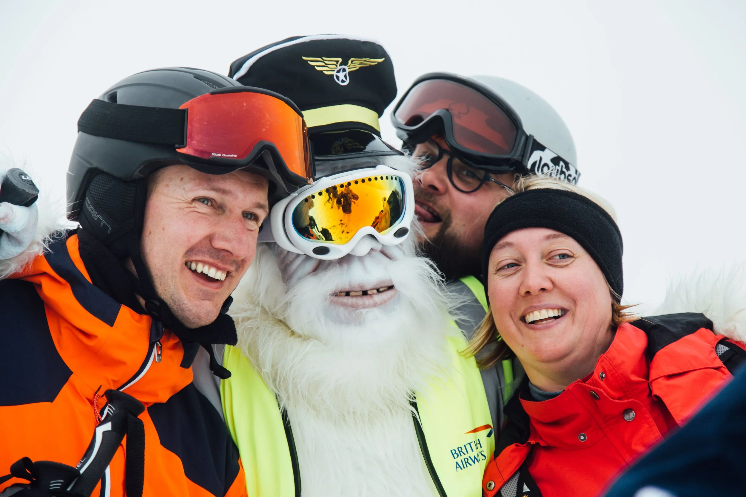 A group of people wearing ski helmets and goggles posing with a person dressed in a yeti costume at a snowy location.