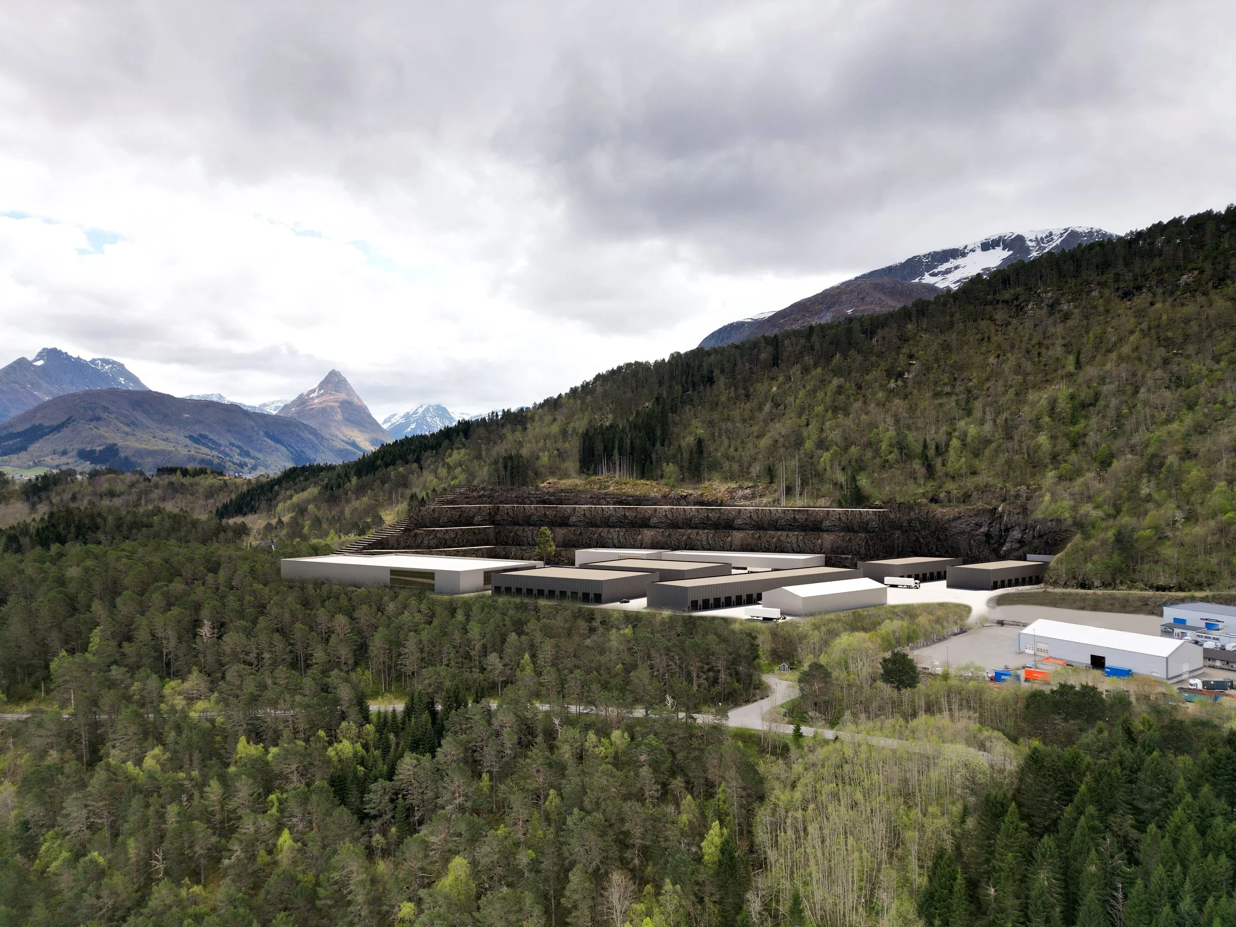 En digital visualisering av et industriområde med lagerbygninger i et fjellandskap med skog og fjell i bakgrunnen.