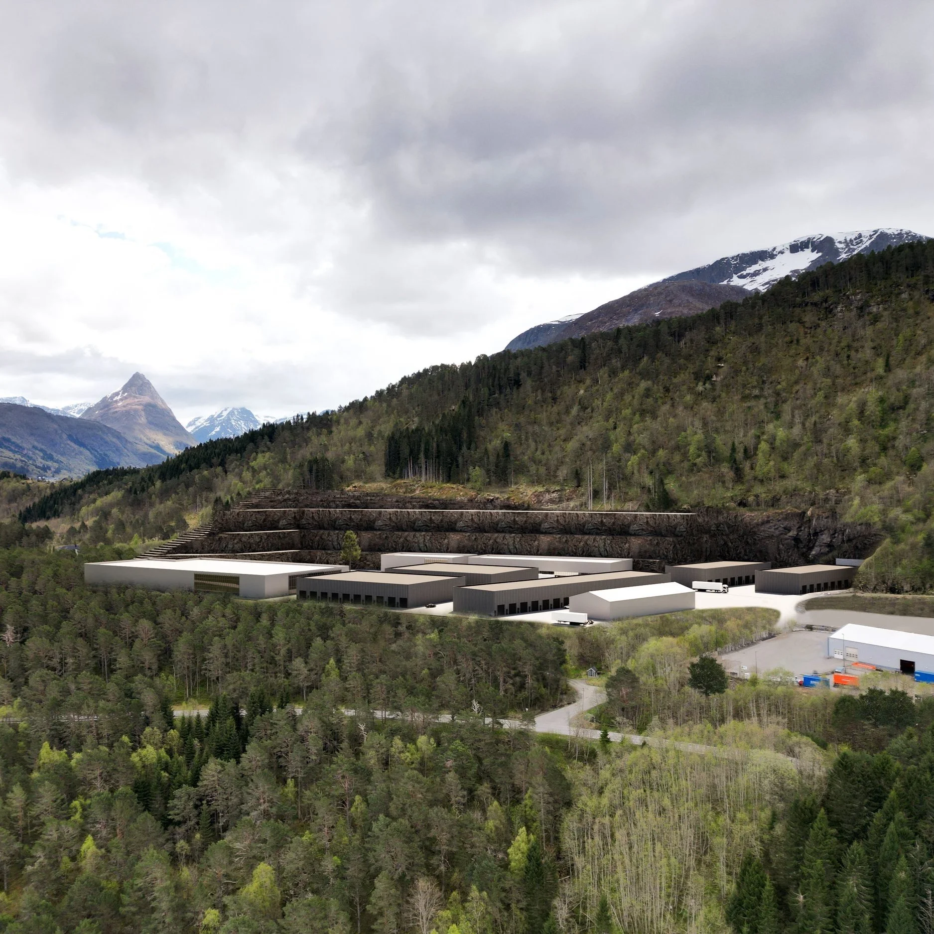 En digital visualisering av et industriområde med lagerbygninger i et fjellandskap med skog og fjell i bakgrunnen.