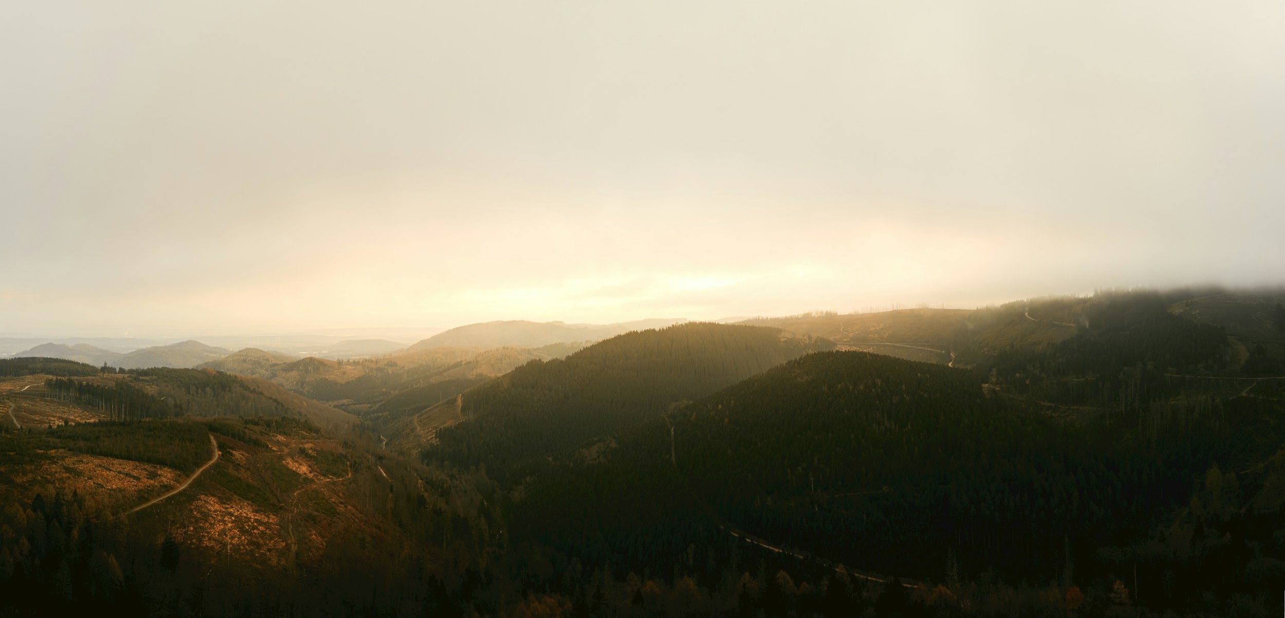 Landschaft mit Hügeln, Wäldern und Straßen bei bewölktem Himmel.