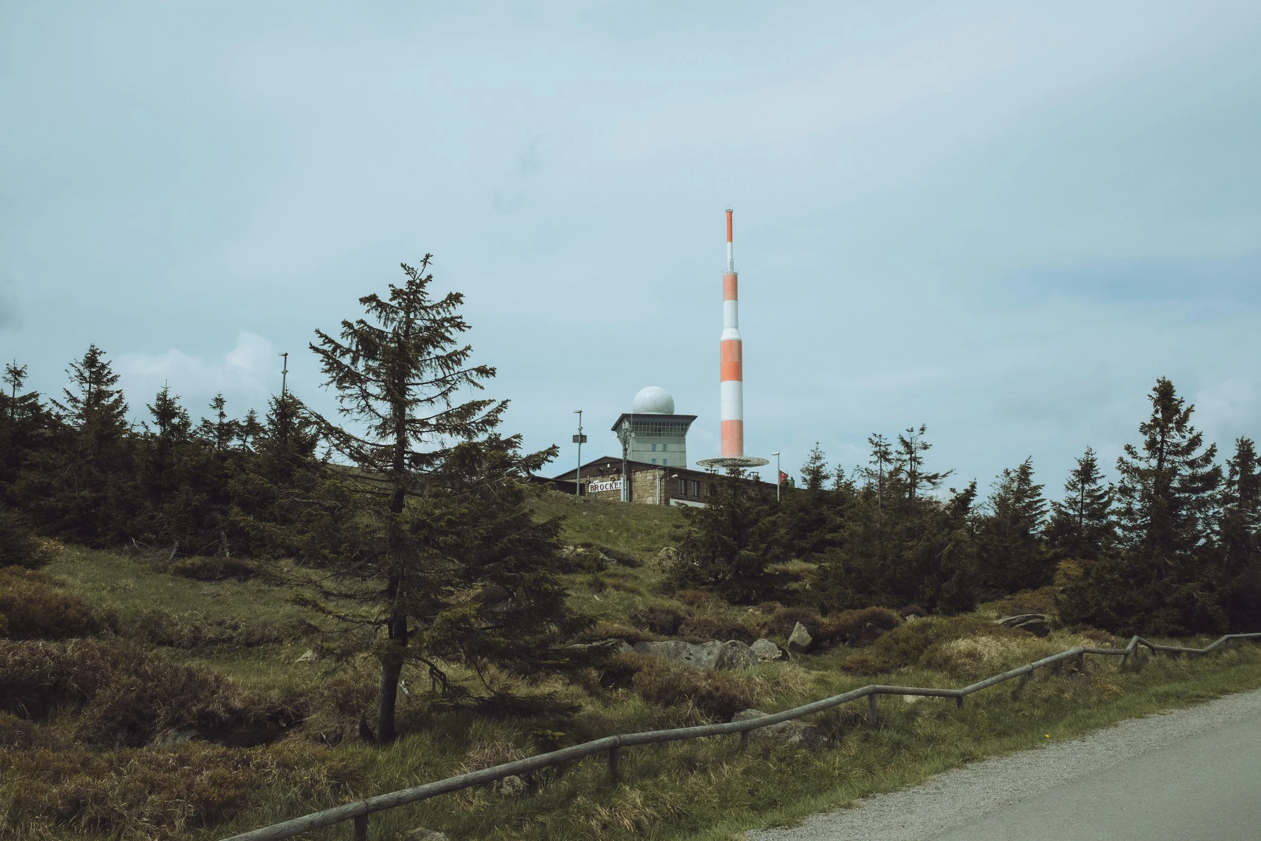 Bergstation mit Kommunikationsantenne, Radar und einem Gebäude, umgeben von Wäldern und Hügeln, unter einem bewölkten Himmel.