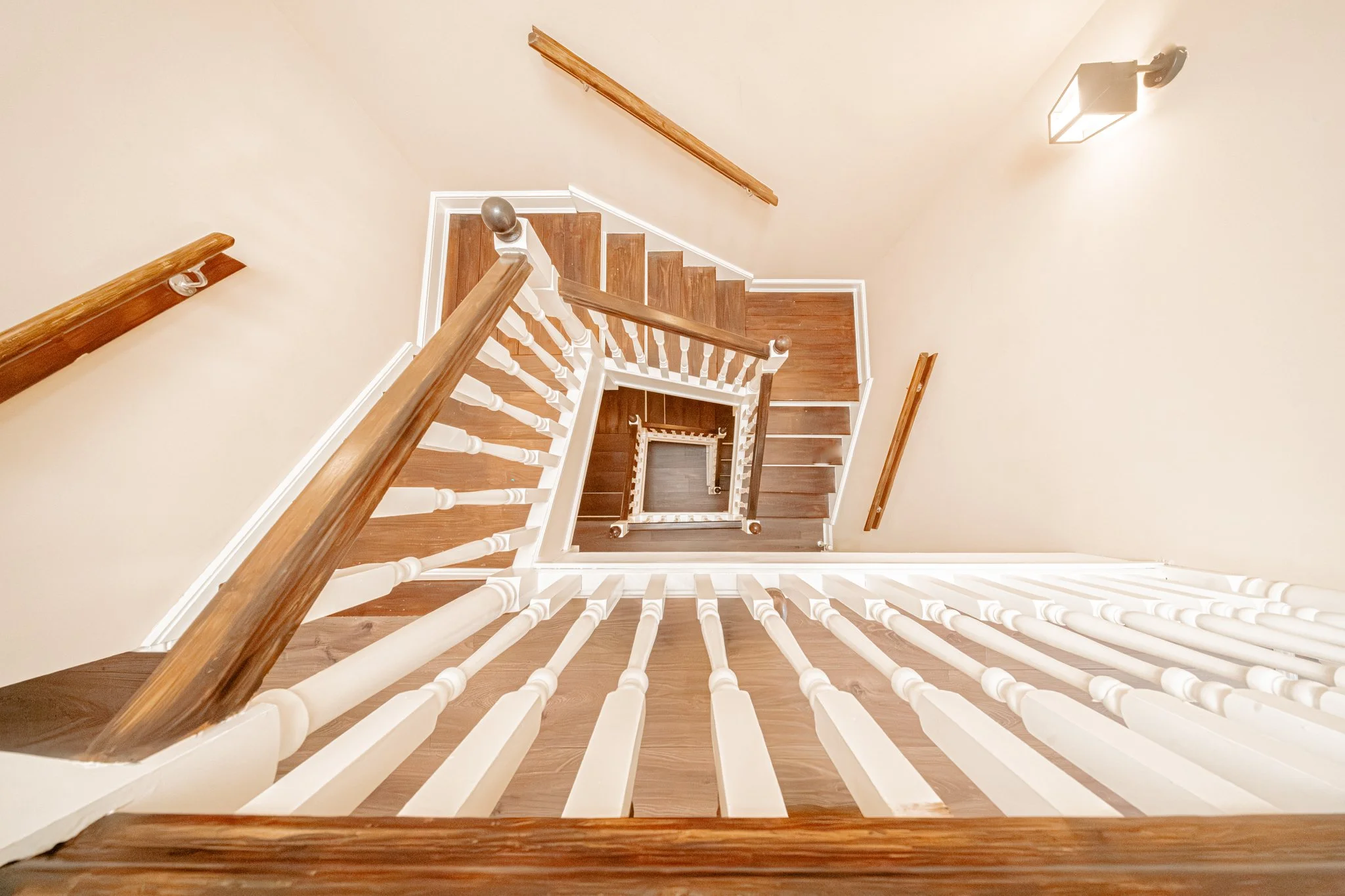 View looking down a staircase with wooden steps, white spindles, and wooden handrails, showing the staircase winding down to a lower level in a home interior.