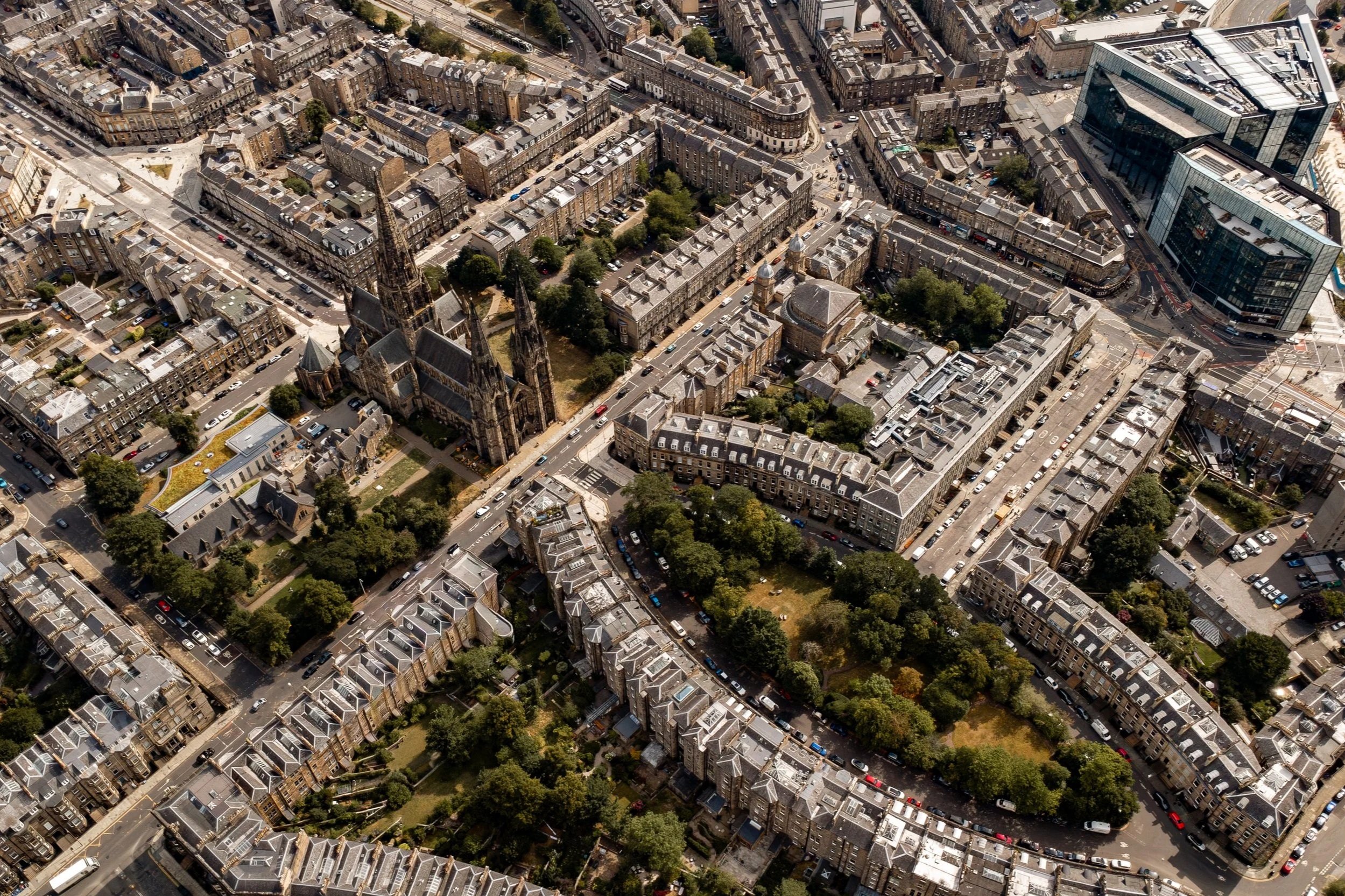 An aerial view of a Edinburgh city center with a large Gothic church, surrounding residential buildings, and some modern buildings, with streets and trees.