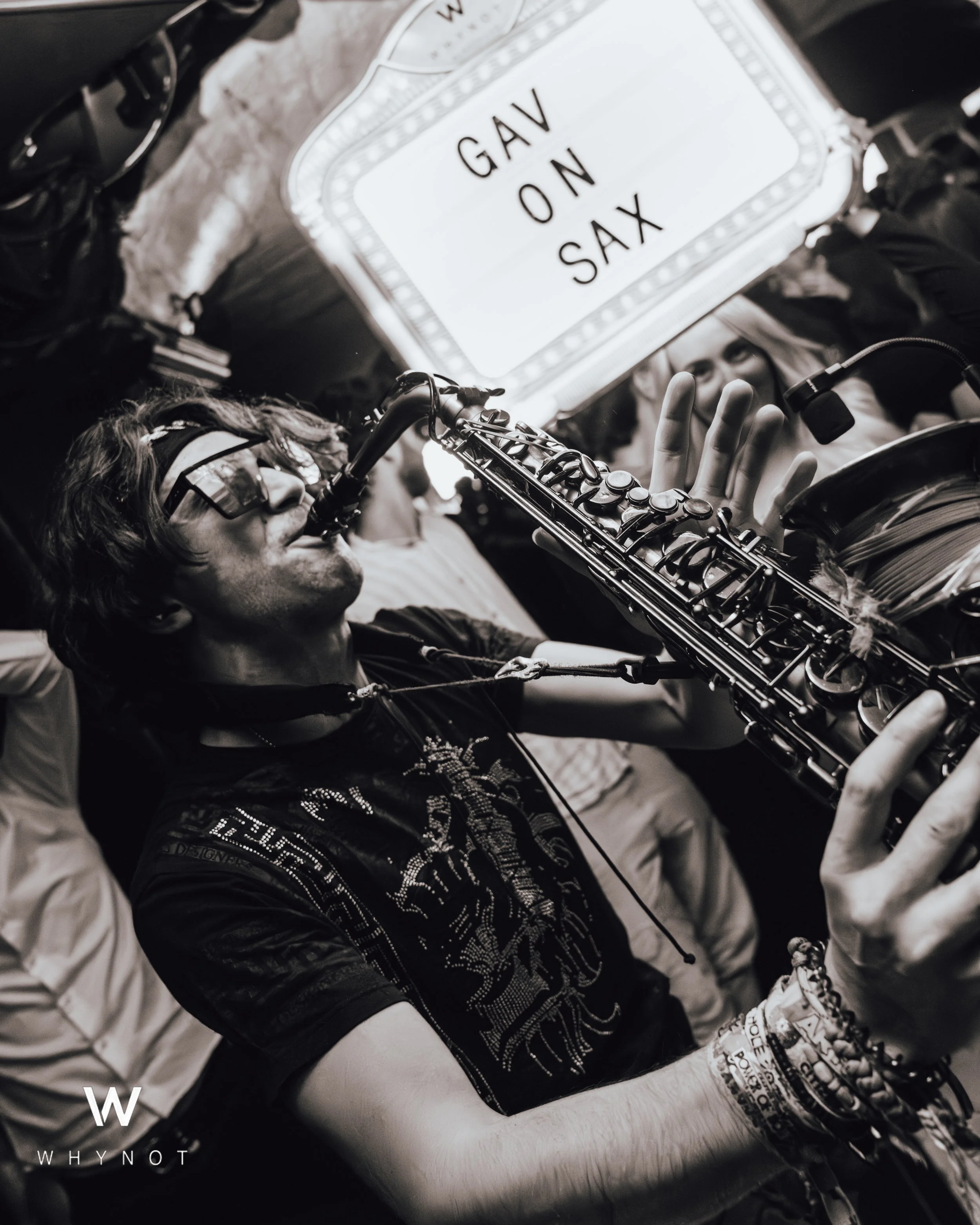 A man playing the saxophone with a sign above him reading 'GAV ON SAX'.