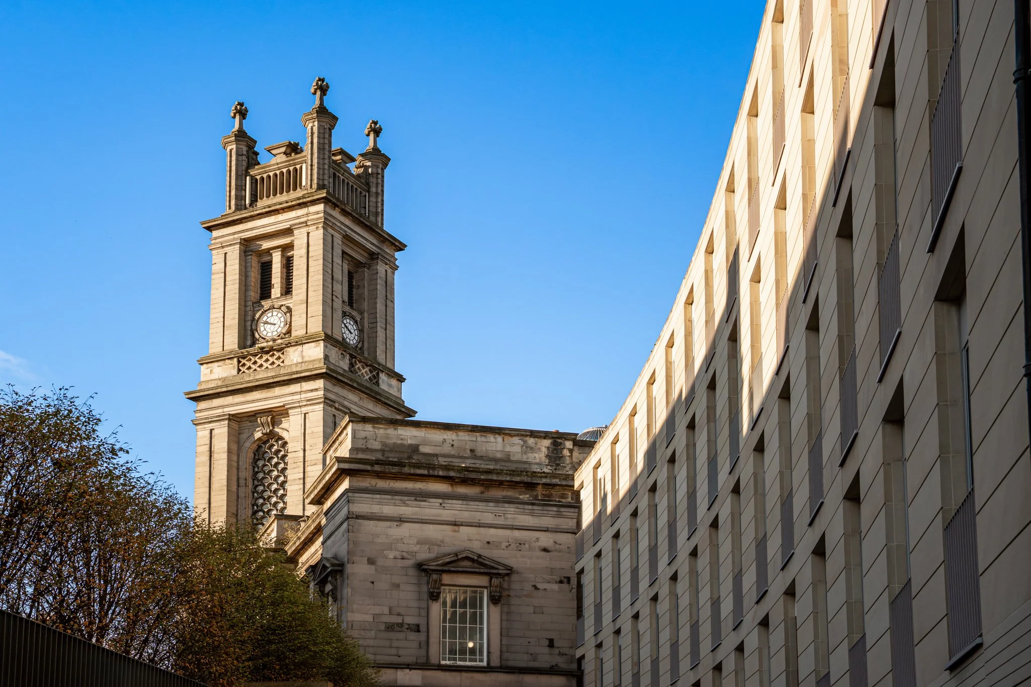 A historic Edinburgh clock tower with Gothic architectural details against a clear blue sky, adjacent to a modern building with rectangular windows. Real Estate
