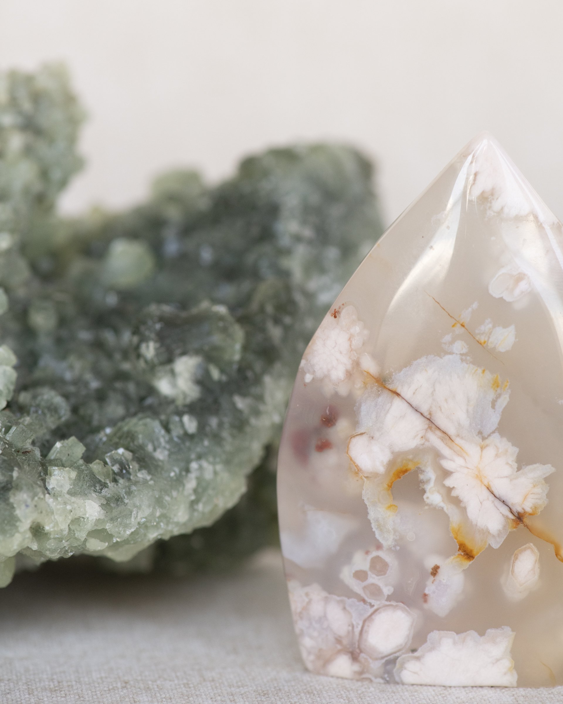 Close-up of a white and orange marbled crystal standing upright, with a blurry green mineral in the background.