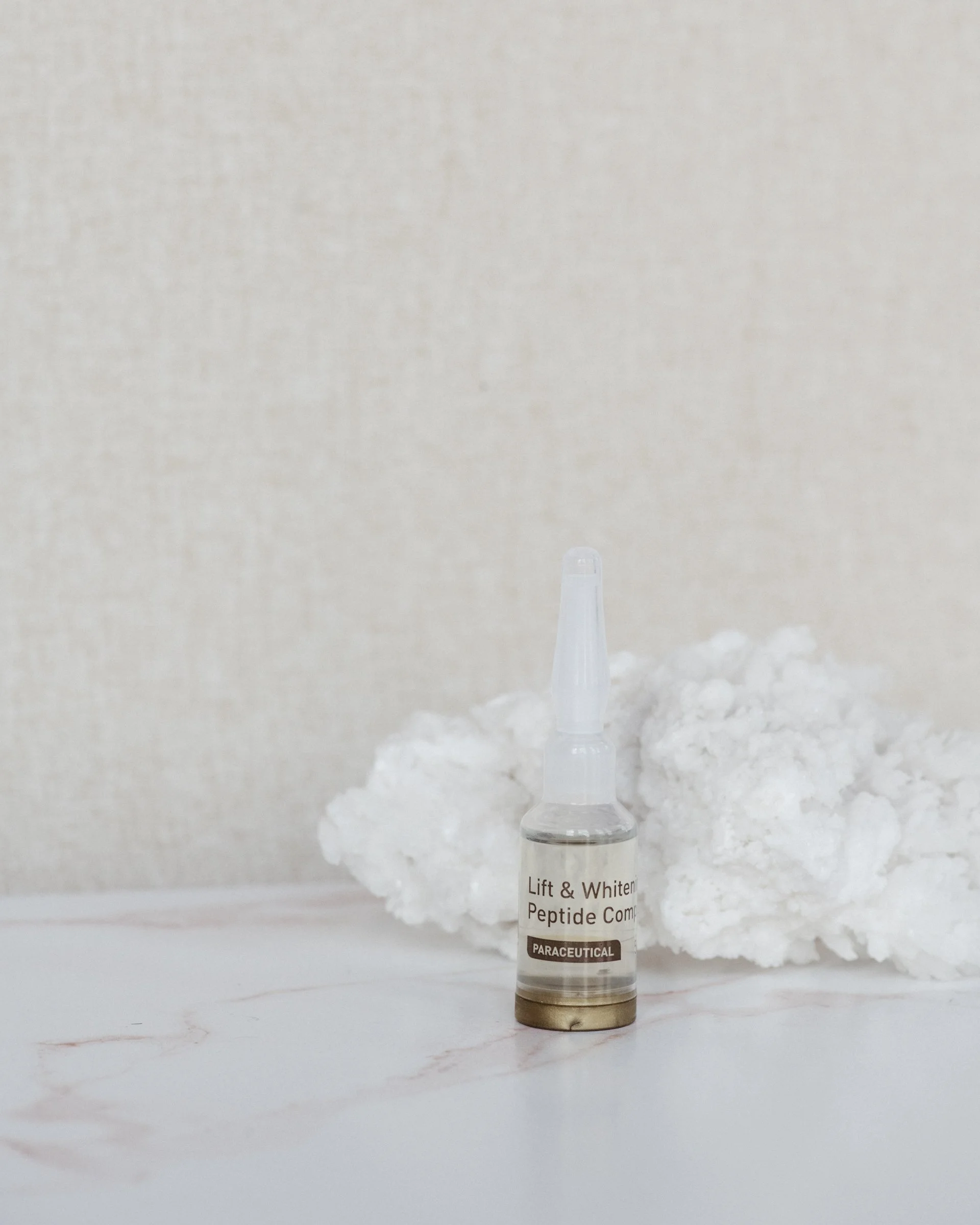 A small clear bottle labeled 'Lift & Whiten Pentine Complex' with a black cap on a white surface, with a plain off-white background.