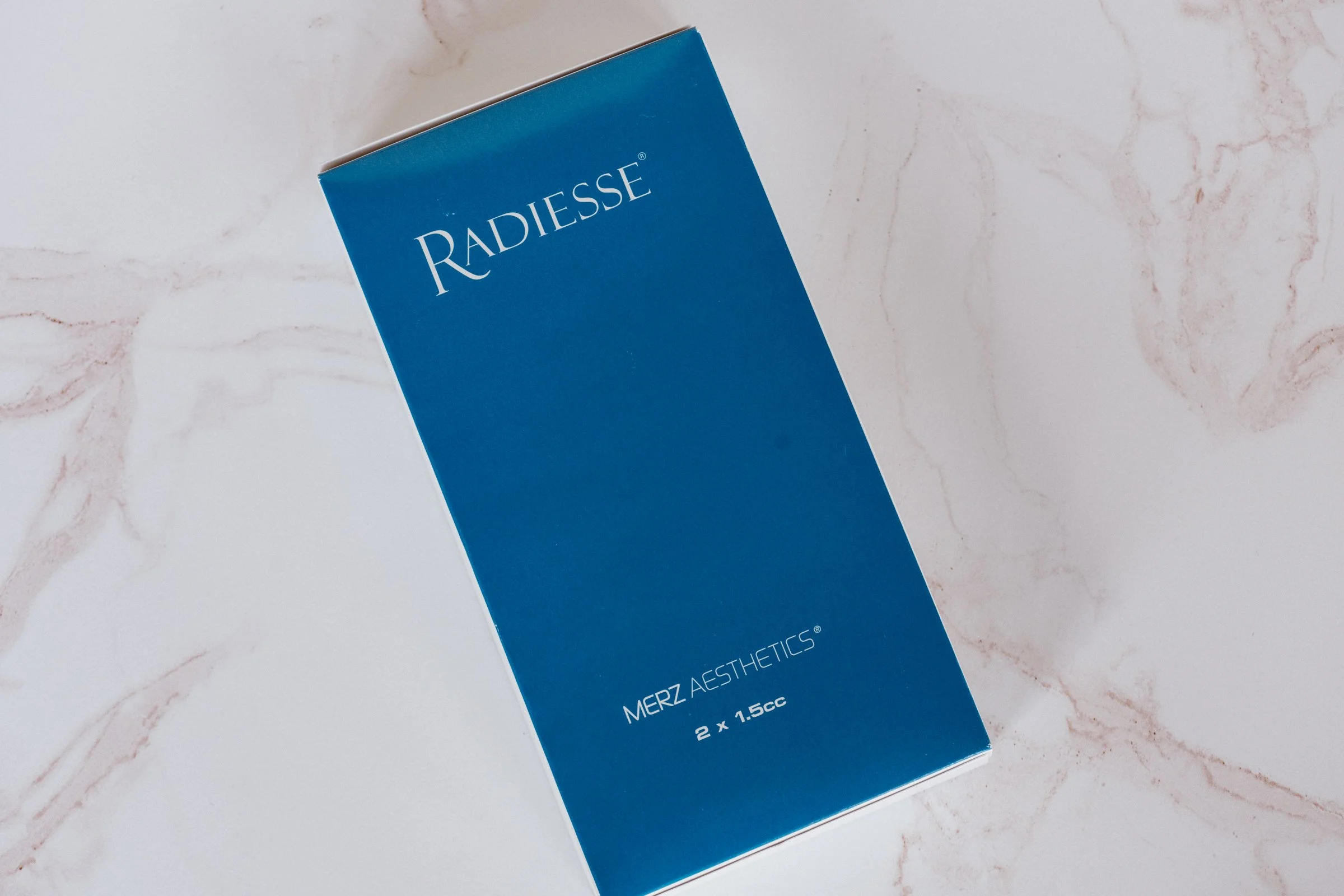 Blue box with white text reading "MERZ AESTHETICS" and additional details, placed on a marble surface.
