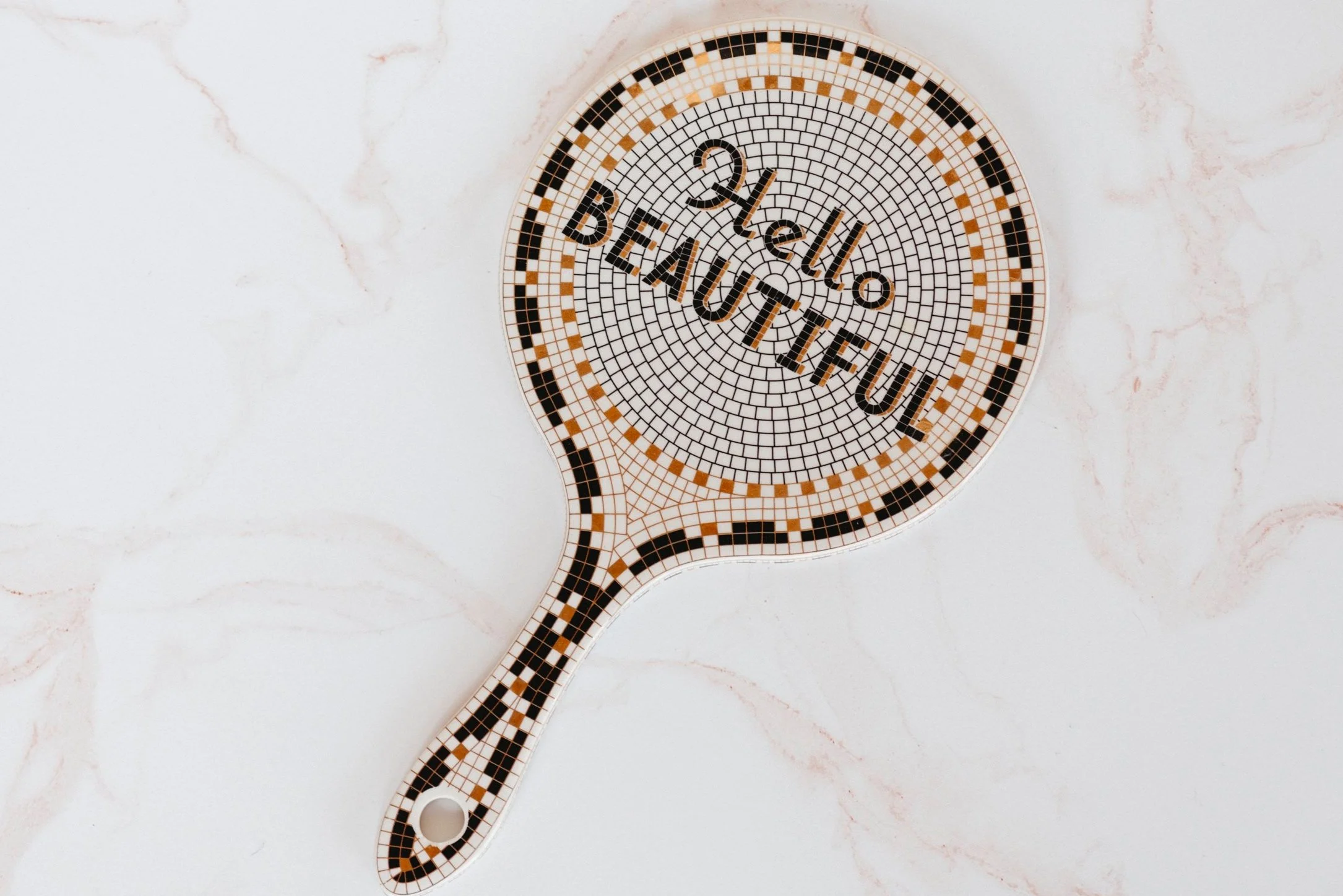 A colorful mosaic stylized mirror with the words 'Be a Kind Human' written across it, placed on a light marble surface.