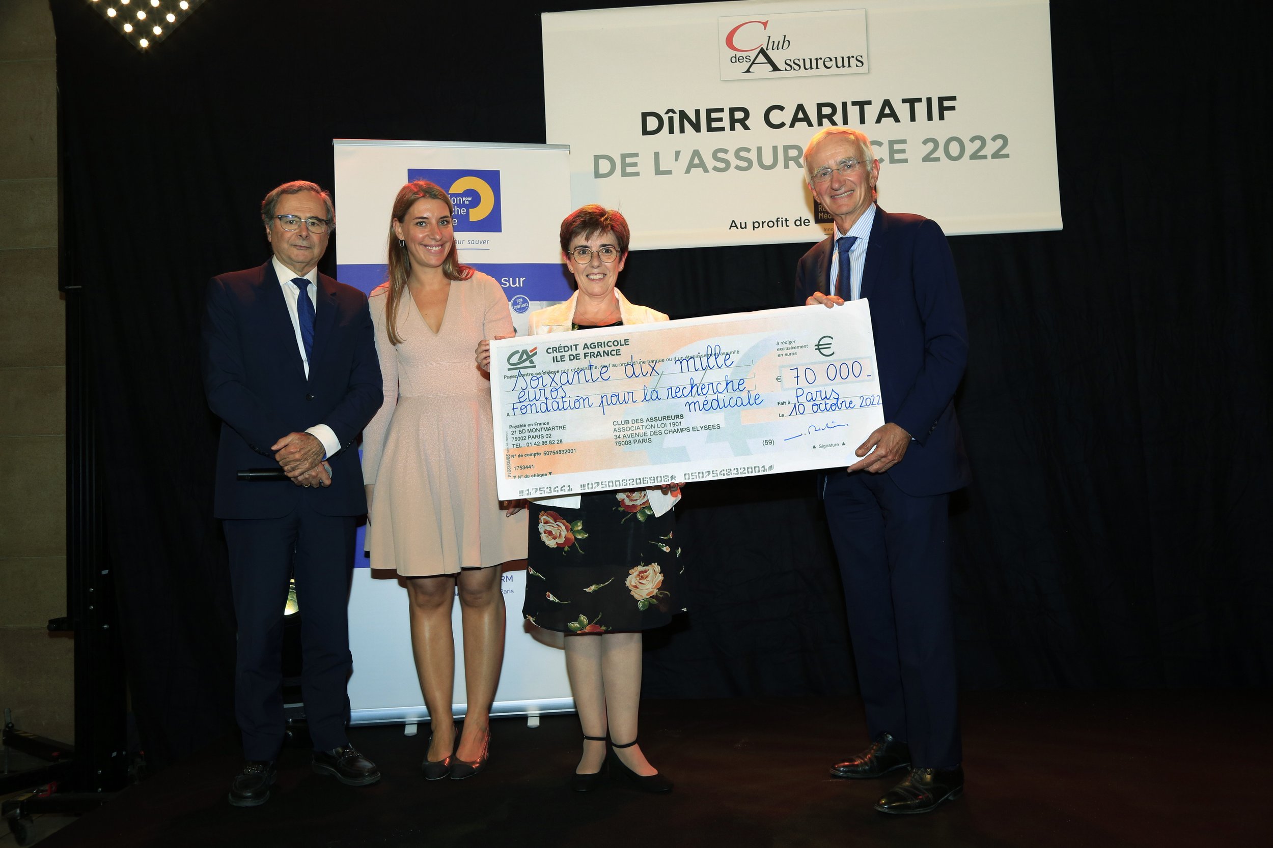 Quatre personnes posent avec un grand chèque lors d'un dîner caritatif de l'assurance en 2022 à Paris. Le chèque, d'un montant de 70 000 euros, est destiné à la recherche médicale.