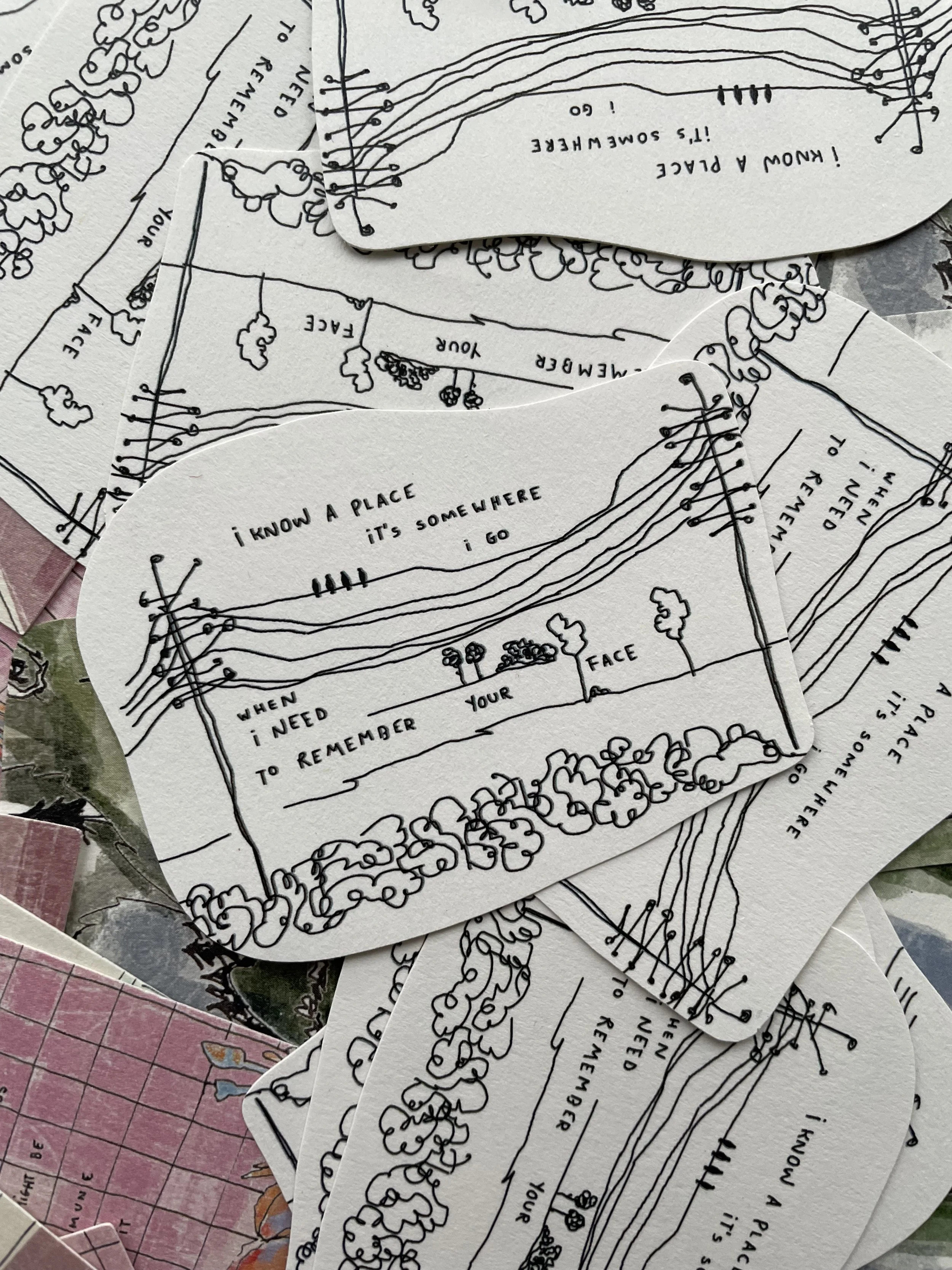 Hand-drawn illustrated cards with poetic lyrics about remembering a place and face, surrounded by trees and nature elements, scattered among other colorful paper items.
