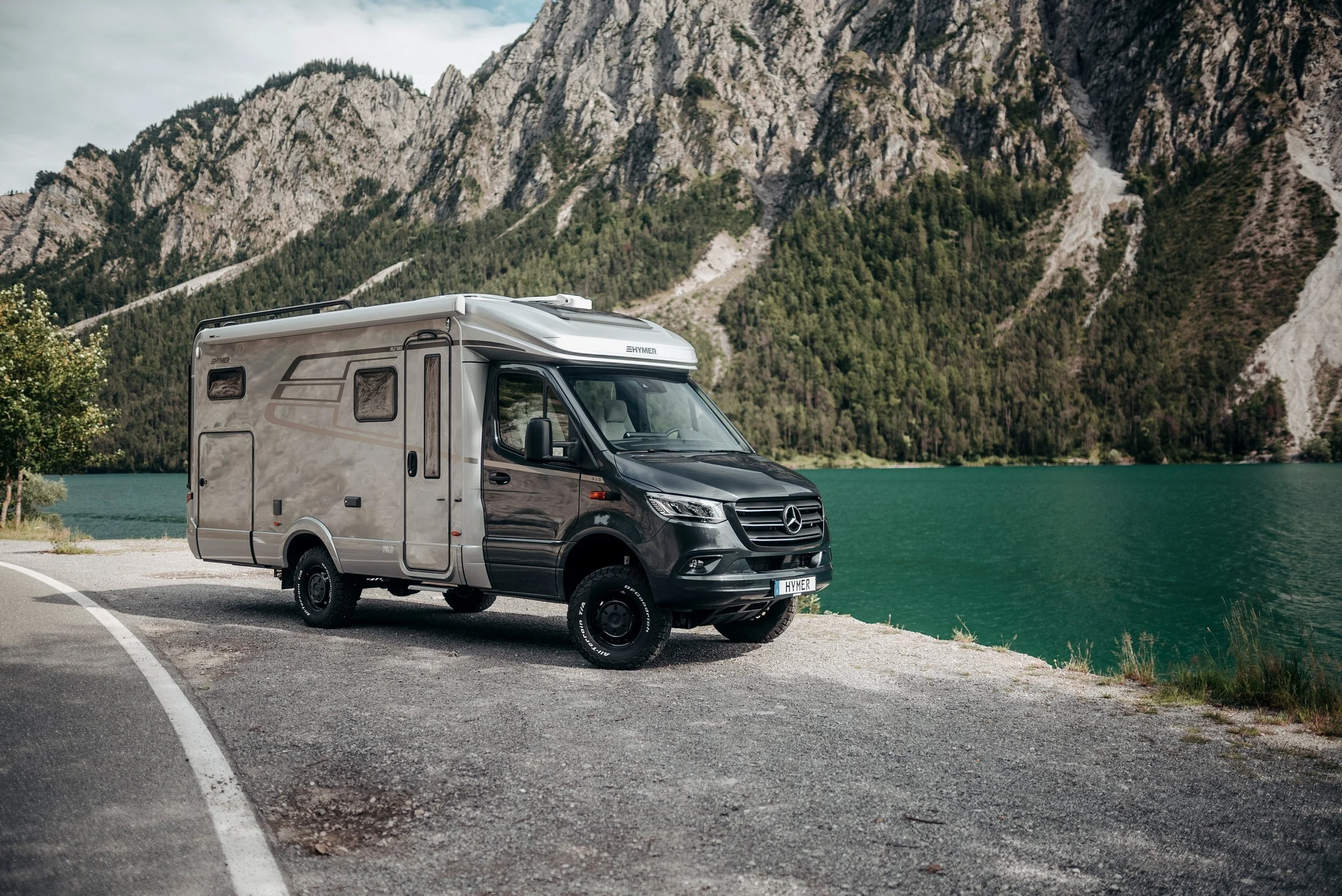 Wohnmobil steht an einem Bergsee, umgeben von Bergen und Wald.