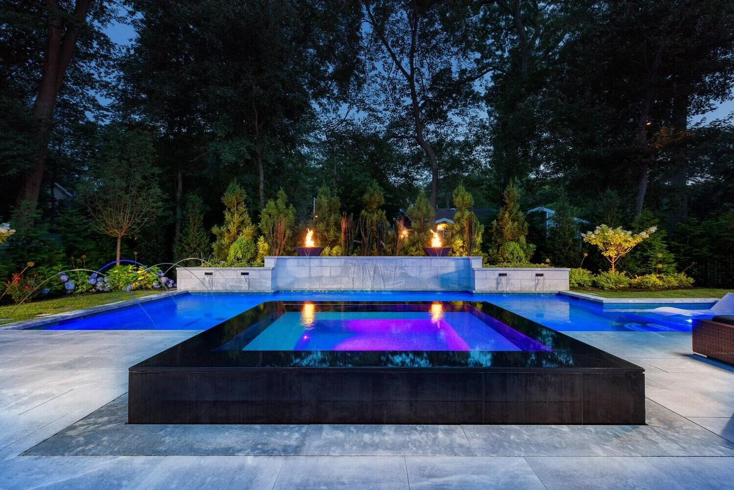 Fiberglass pool with attached spa, fire features, and retaining wall with waterfall