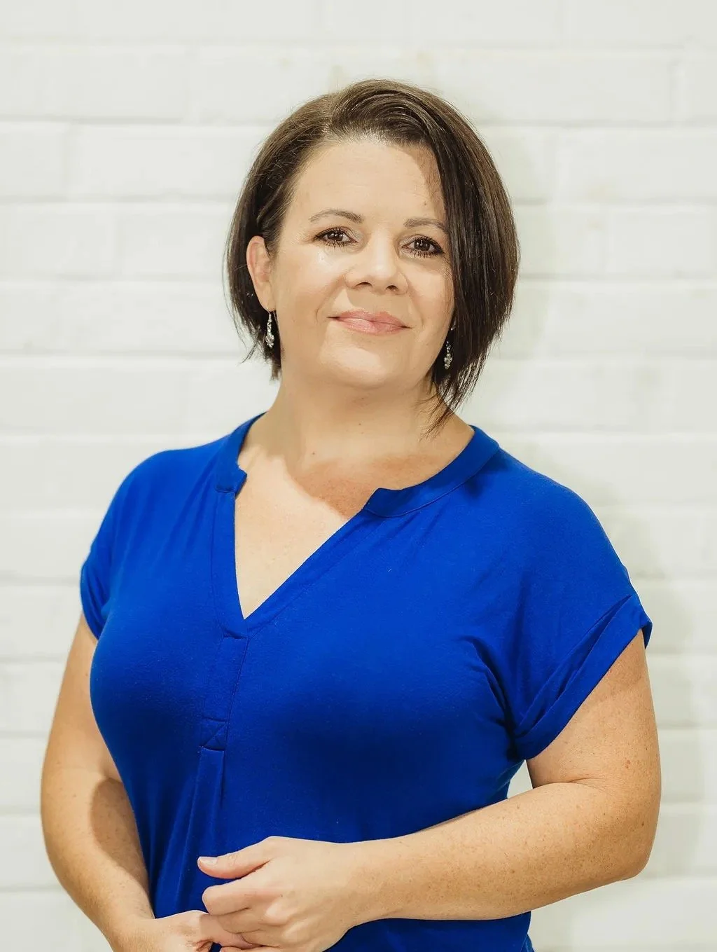 Woman in blue shirt standing against a white brick wall.