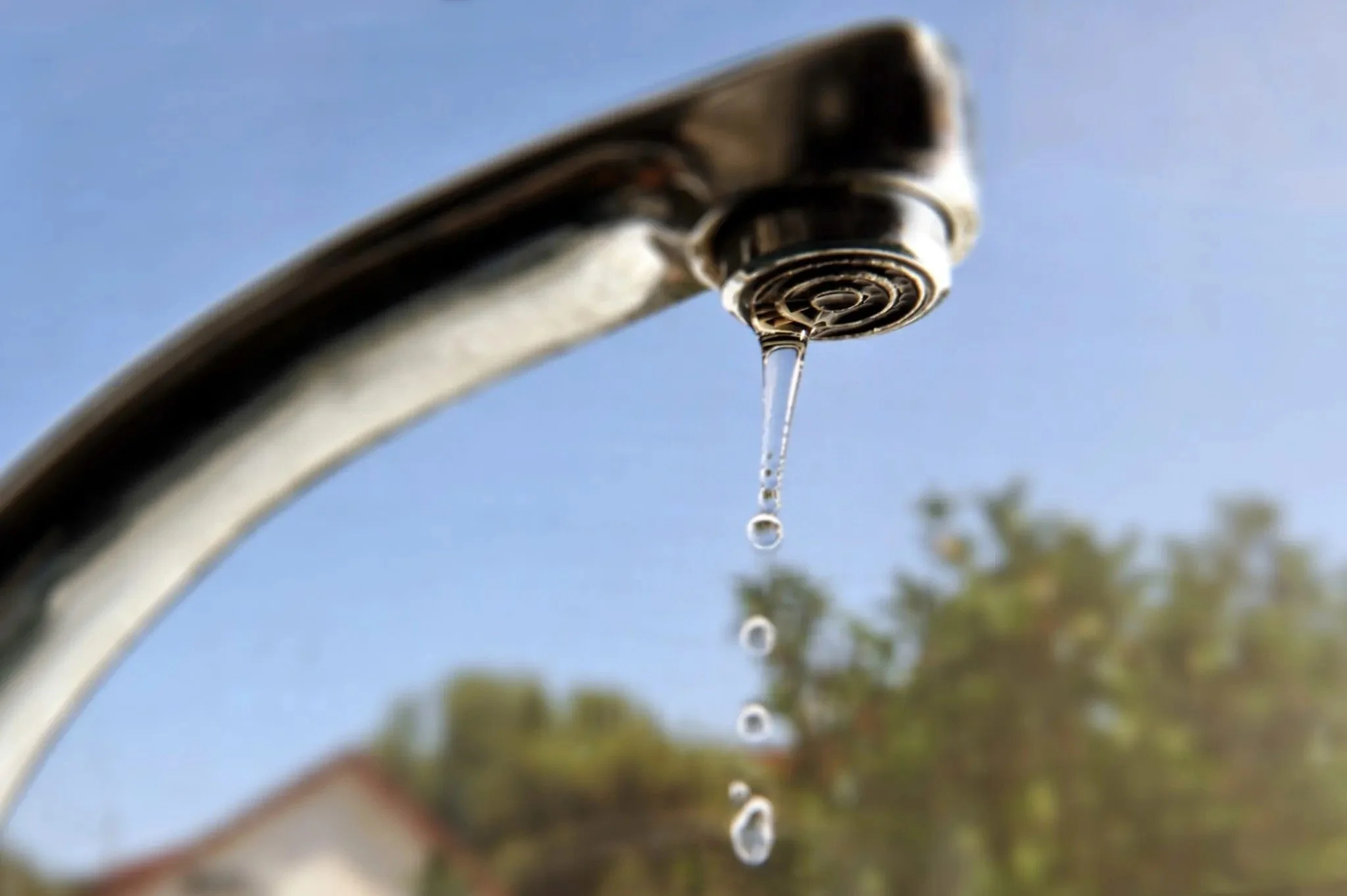 Close-up of a dripping faucet with water droplets against a blurred outdoor background.