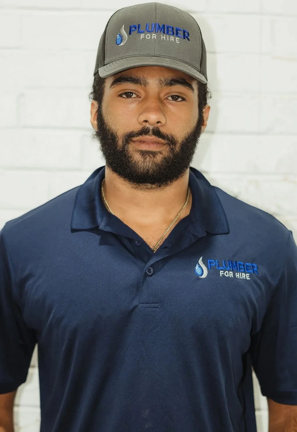 A person wearing a cap and polo shirt with 'Plumber for Hire' logo.