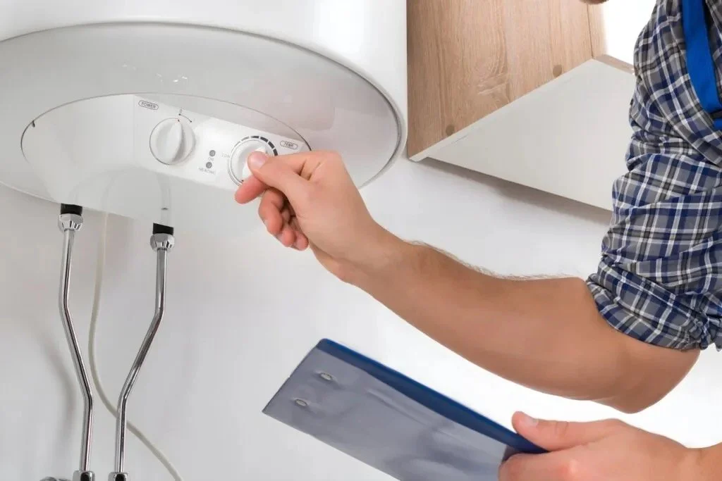 Person adjusting thermostat on white water heater in utility room.