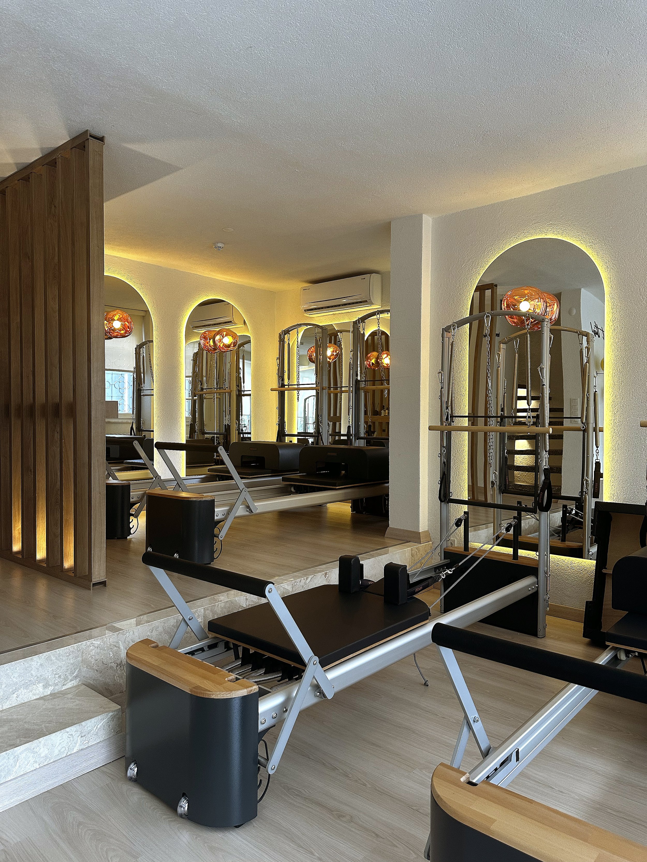 Modern bir pilates stüdyosu, reformer makineleri ve büyük aynalarla döşenmiş aydınlık bir iç mekan.