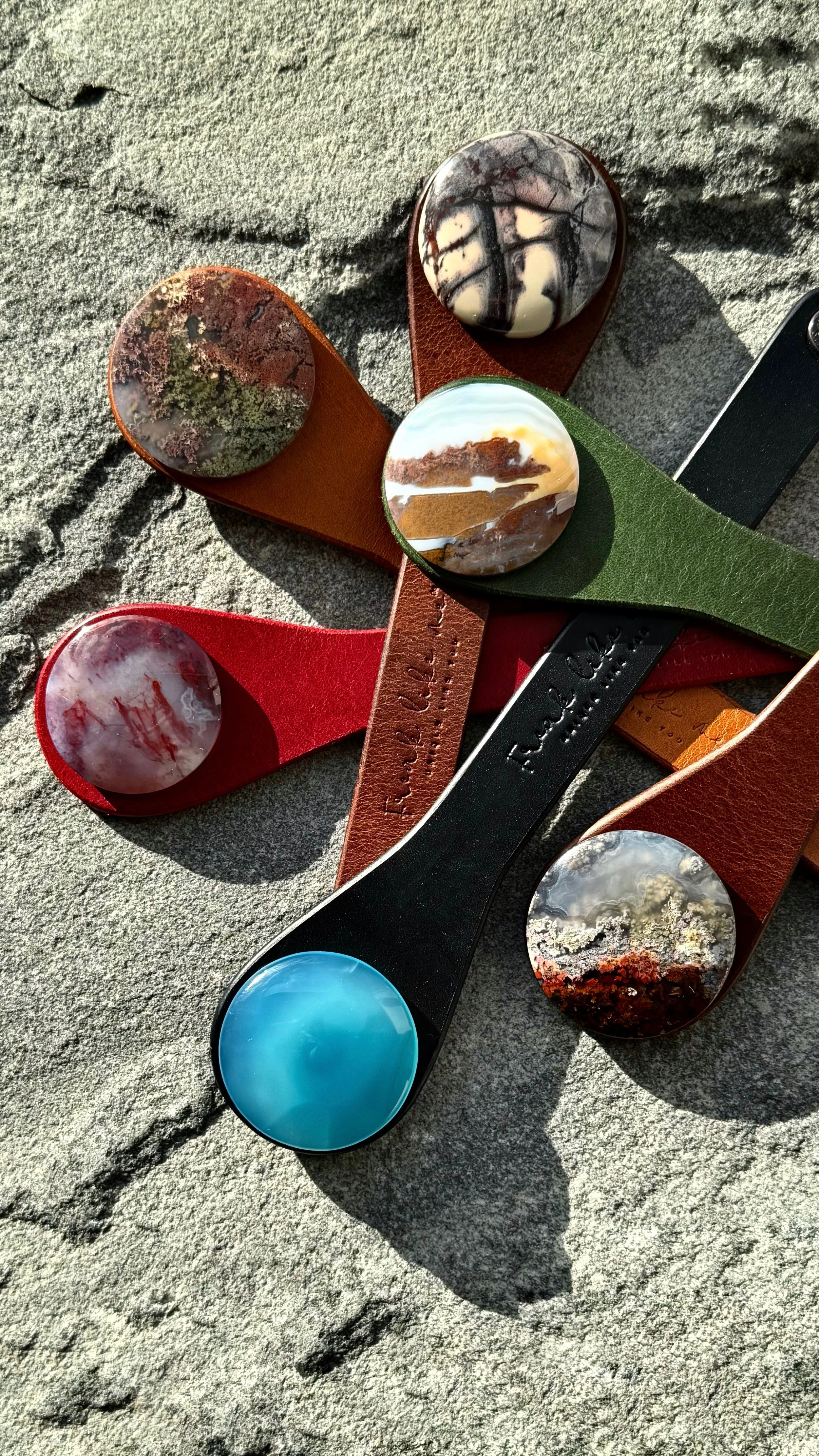 Colorful leather straps with circular gemstone embellishments laid on a textured surface.