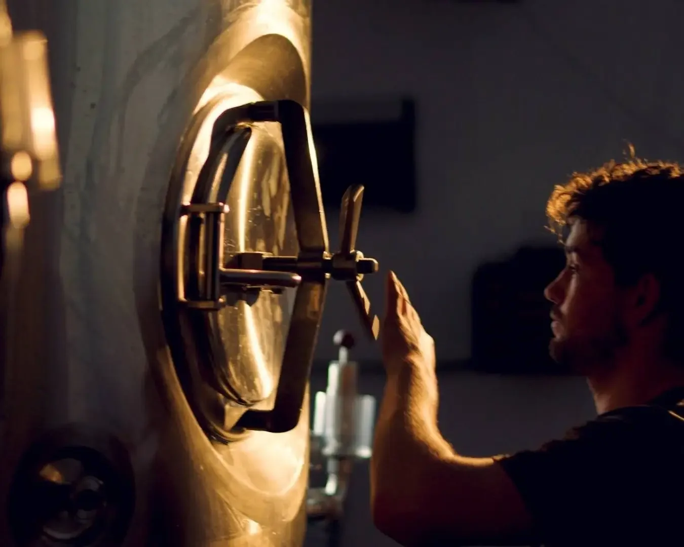 A man with curly hair and beard touching a giant golden clock with both hands in a dimly lit room.