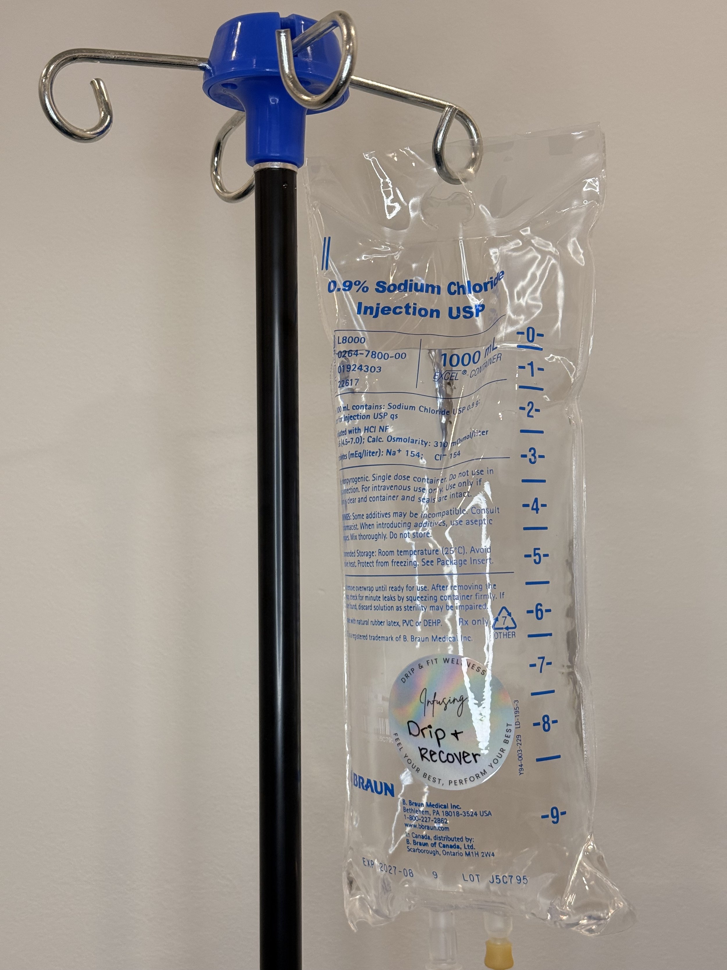 A hospital IV drip bag filled with 0.9% sodium chloride injection hanging from a black pole with a blue top, against a plain wall.