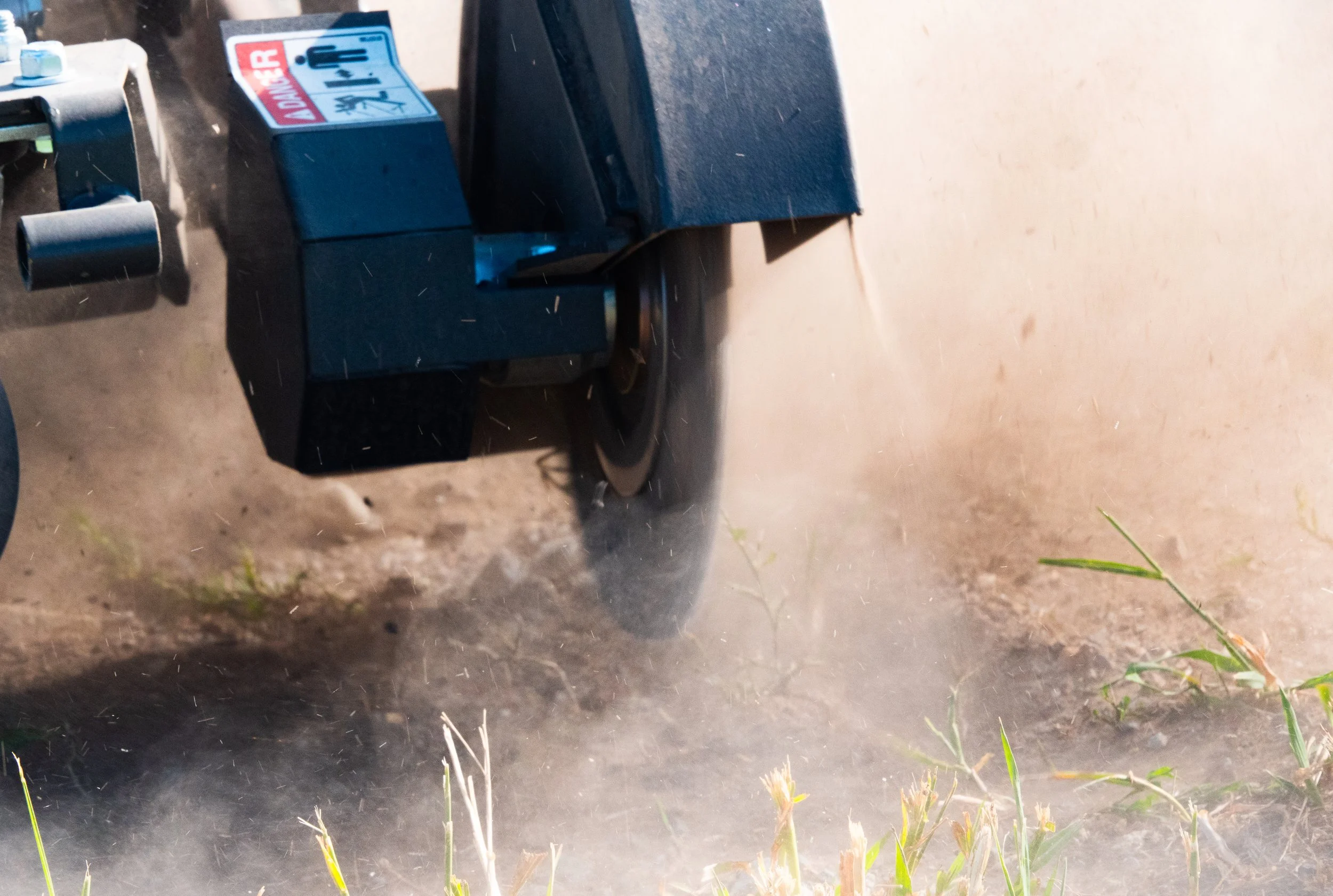 Close-up of a power tiller or cultivator working on a dirt patch, stirring up dust and small plants.