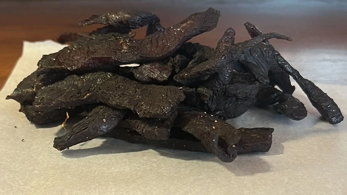 Pile of dark brown beef jerky on parchment paper.