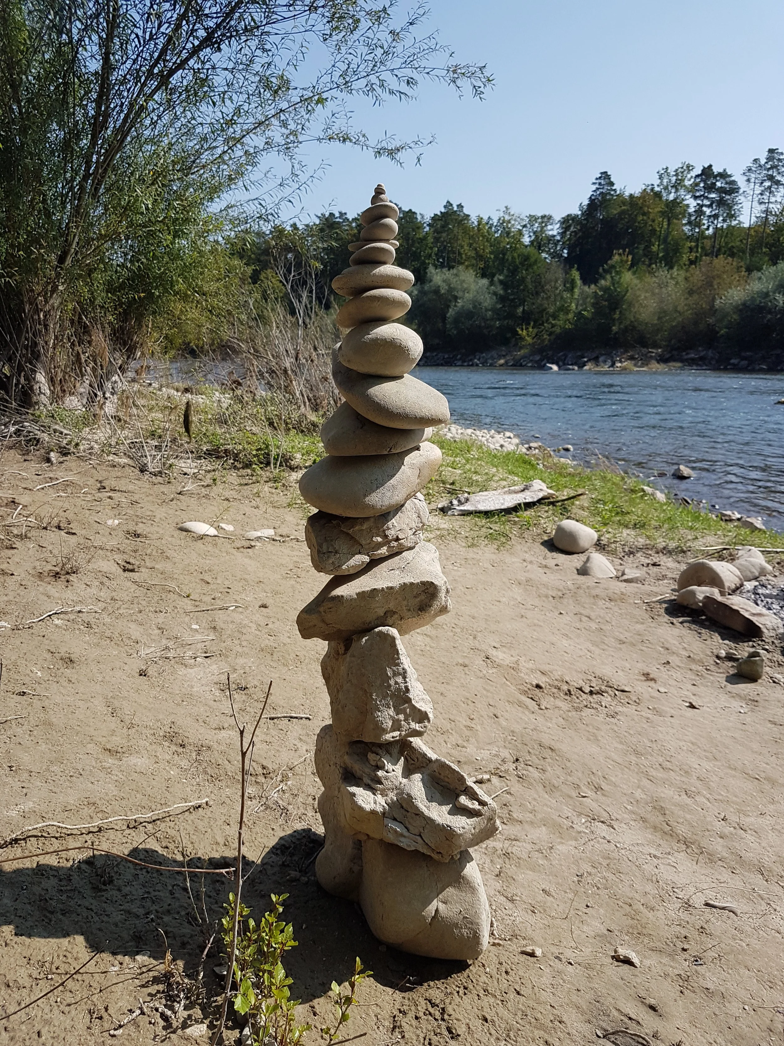 Ein Turm aus flachen Steinen am Flussufer in der Natur, mit Bäumen im Hintergrund.