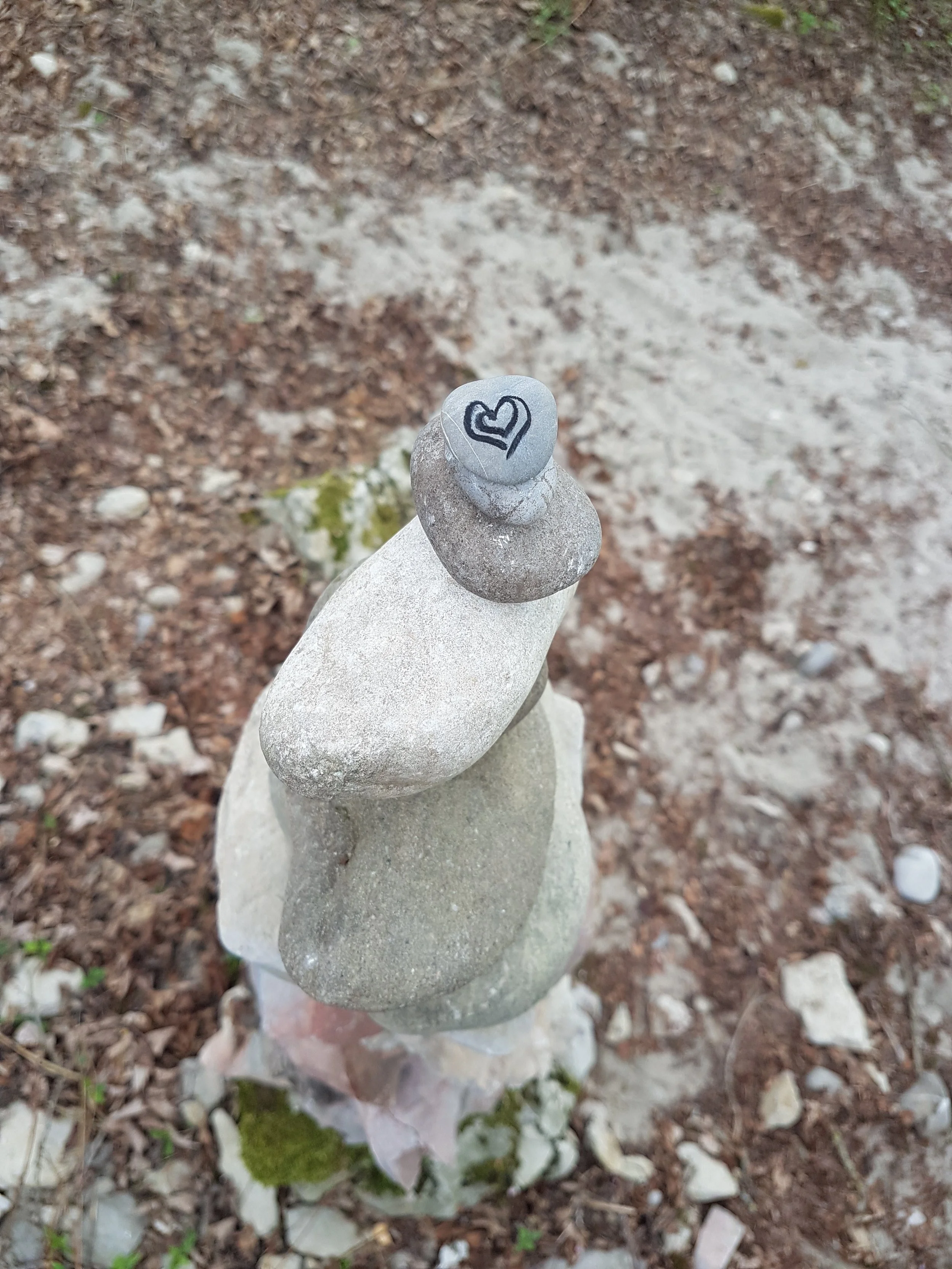 Aufgestapelte Steine auf einem Boden mit Erde und kleinen Steinen, Spitze hat ein Herz mit Pfeil gezeichnet.